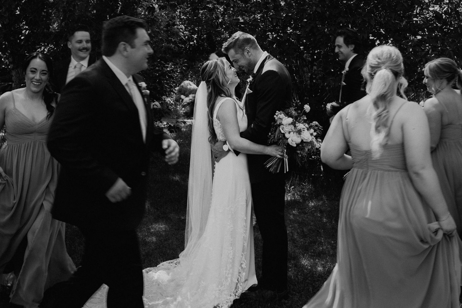 Black and white wedding ceremony photo showing exchange of vows in an outdoor garden setting.
