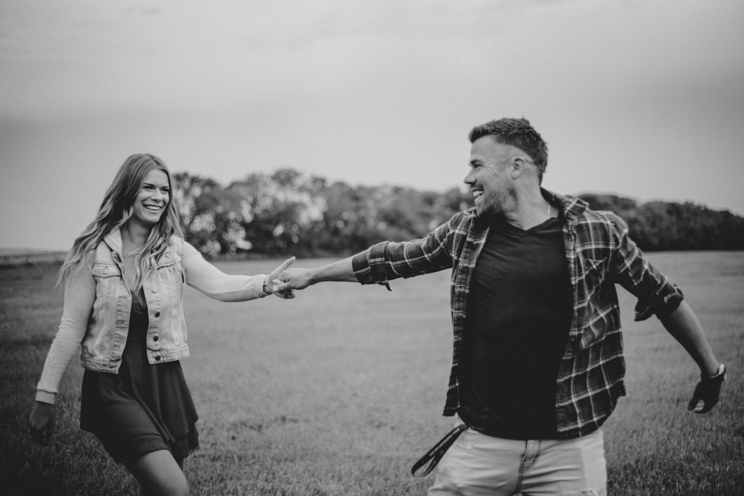A couple holds hands while walking through a green field in black and white.