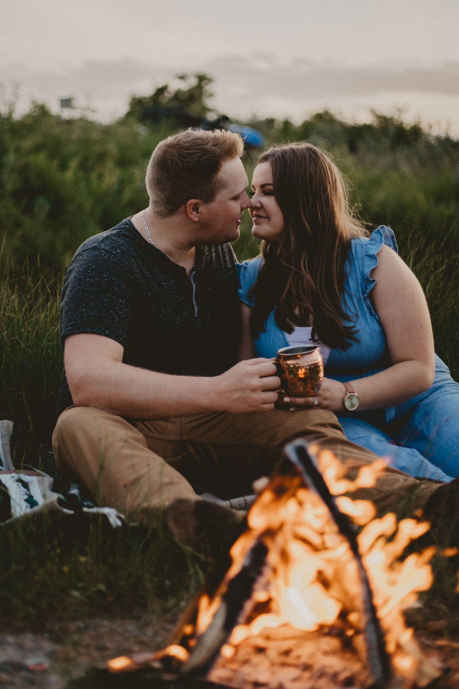 Couple sharing intimate moment by glowing campfire during sunset.