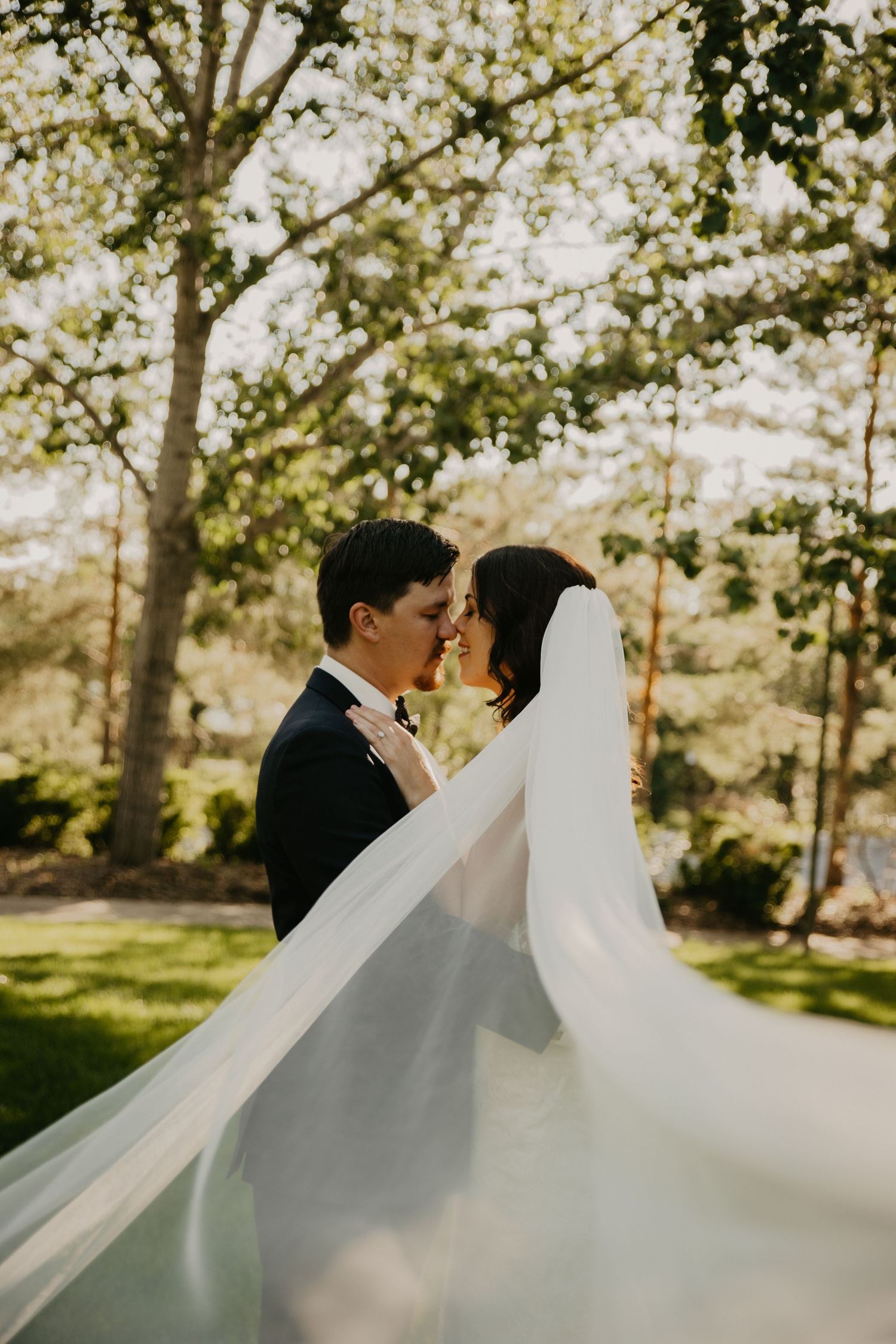 Artistic wedding photo with flowing veil capturing intimate moment in garden setting.