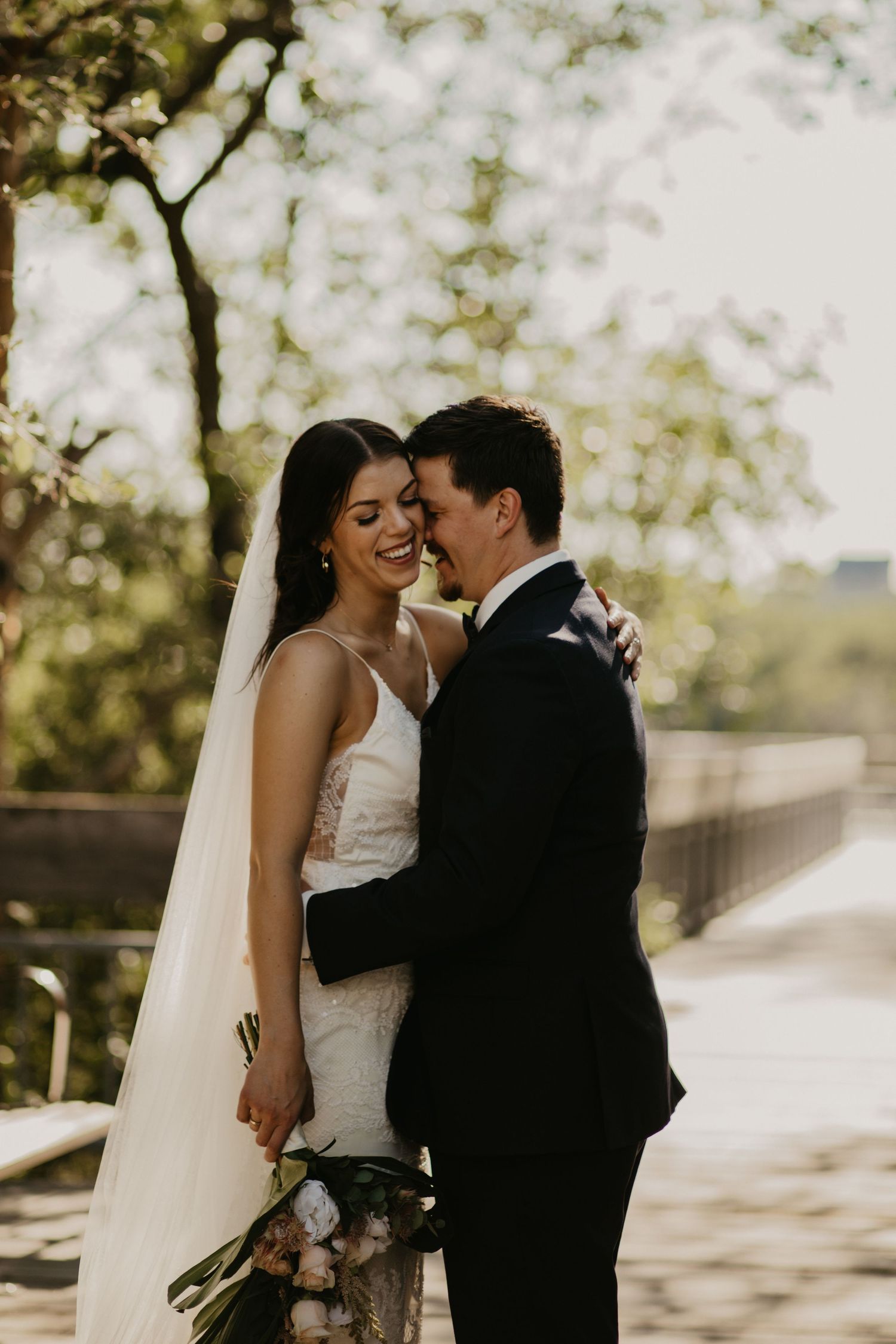 A joyful wedding moment captured outdoors with natural lighting and a long flowing veil.