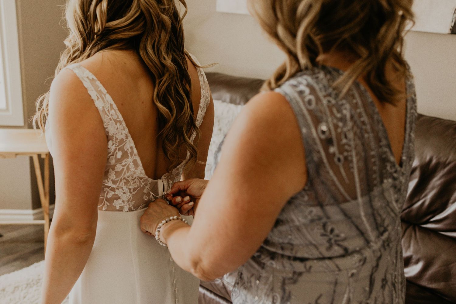 Back view of bride being helped into wedding dress with lace and button details.