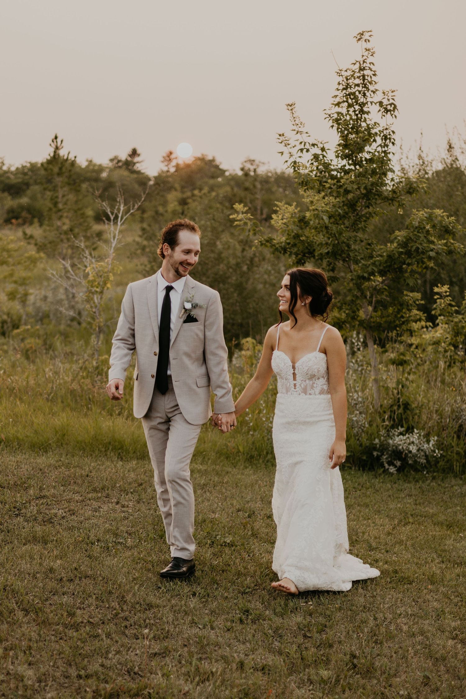Couple walks hand in hand through golden field during sunset wedding portraits.