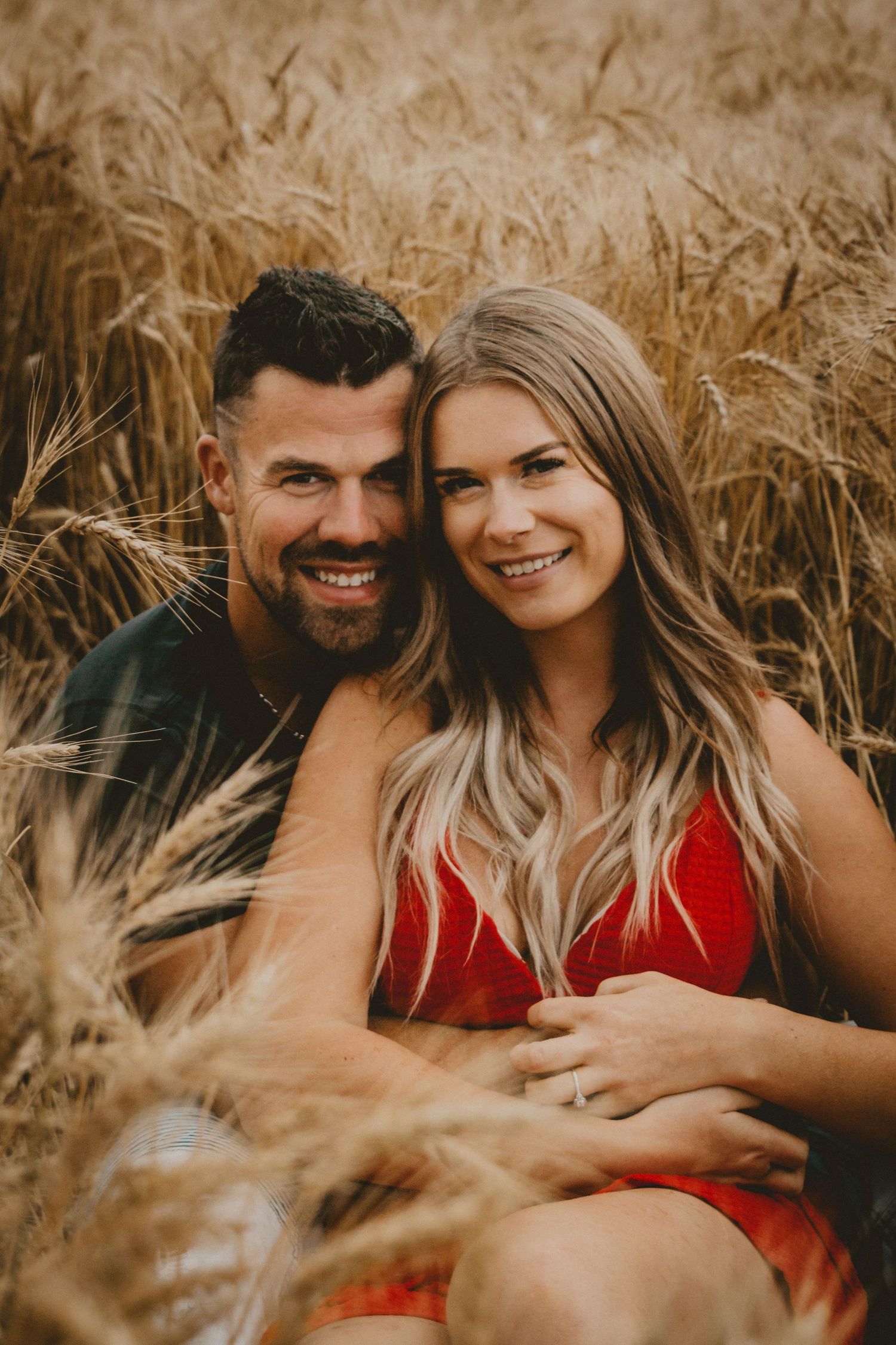A couple shares joyful laughter while sitting in tall golden wheat.