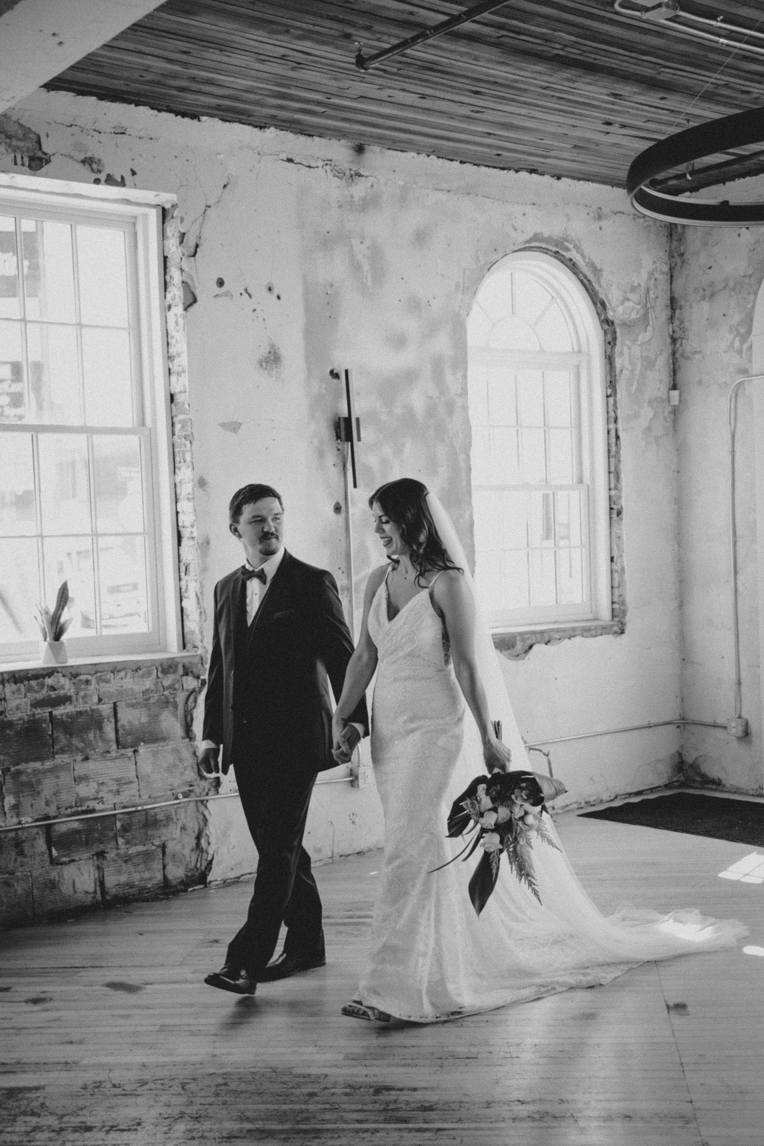 Black and white wedding photo in an industrial style room with arched windows and wooden floors.