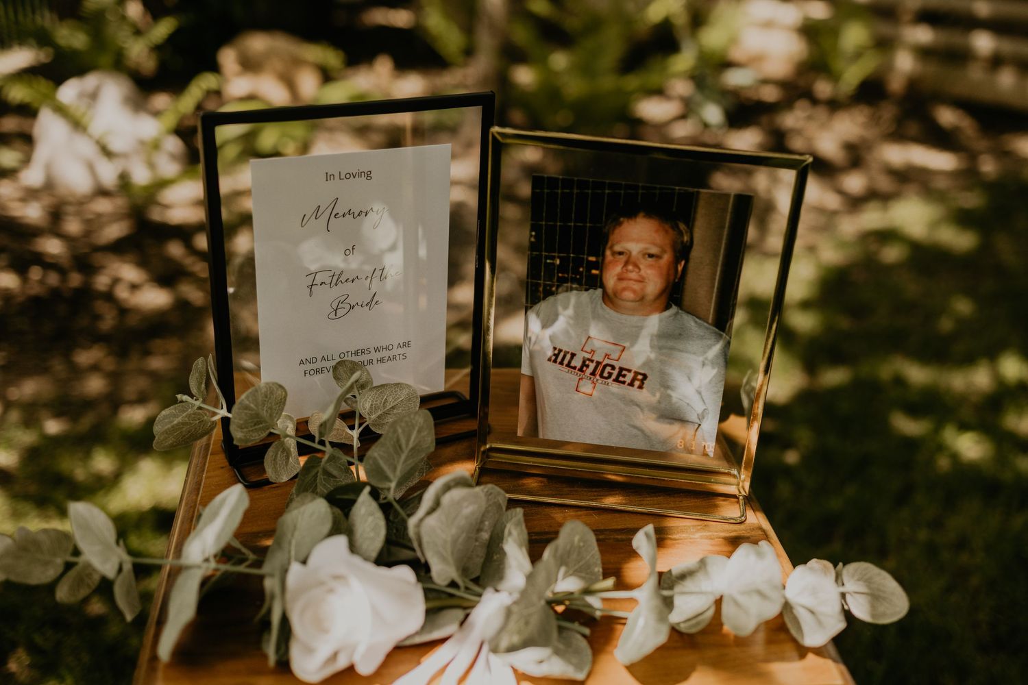Wedding memorial display with framed photos and floral decorations in outdoor garden setting.