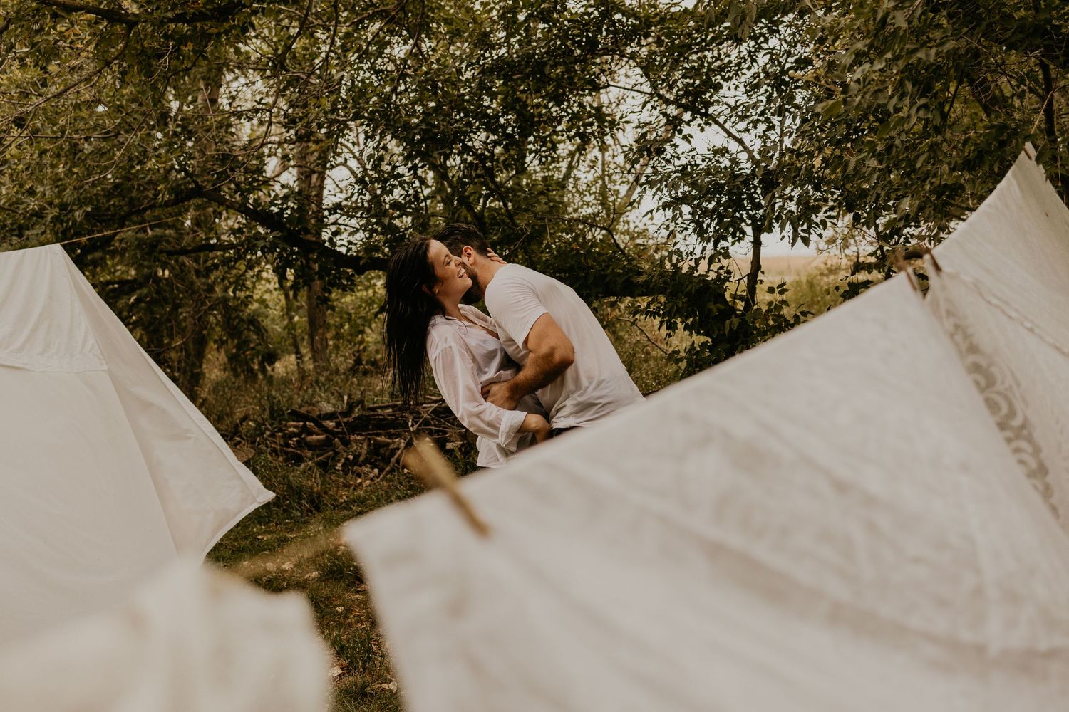 A romantic scene between white sheets hanging outdoors with sunlight filtering through.