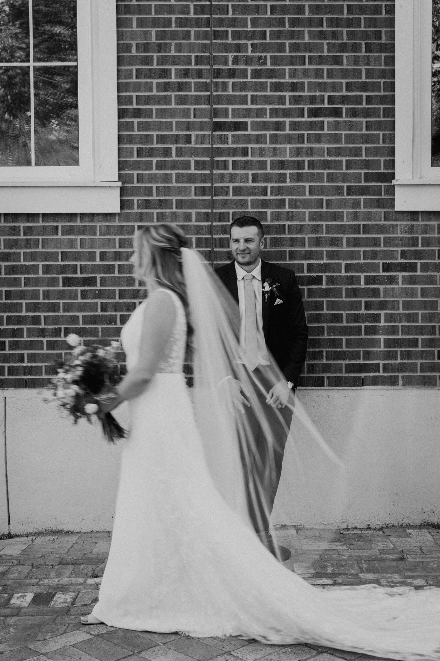 A black and white wedding photo of a couple sharing a candid moment against a brick wall.