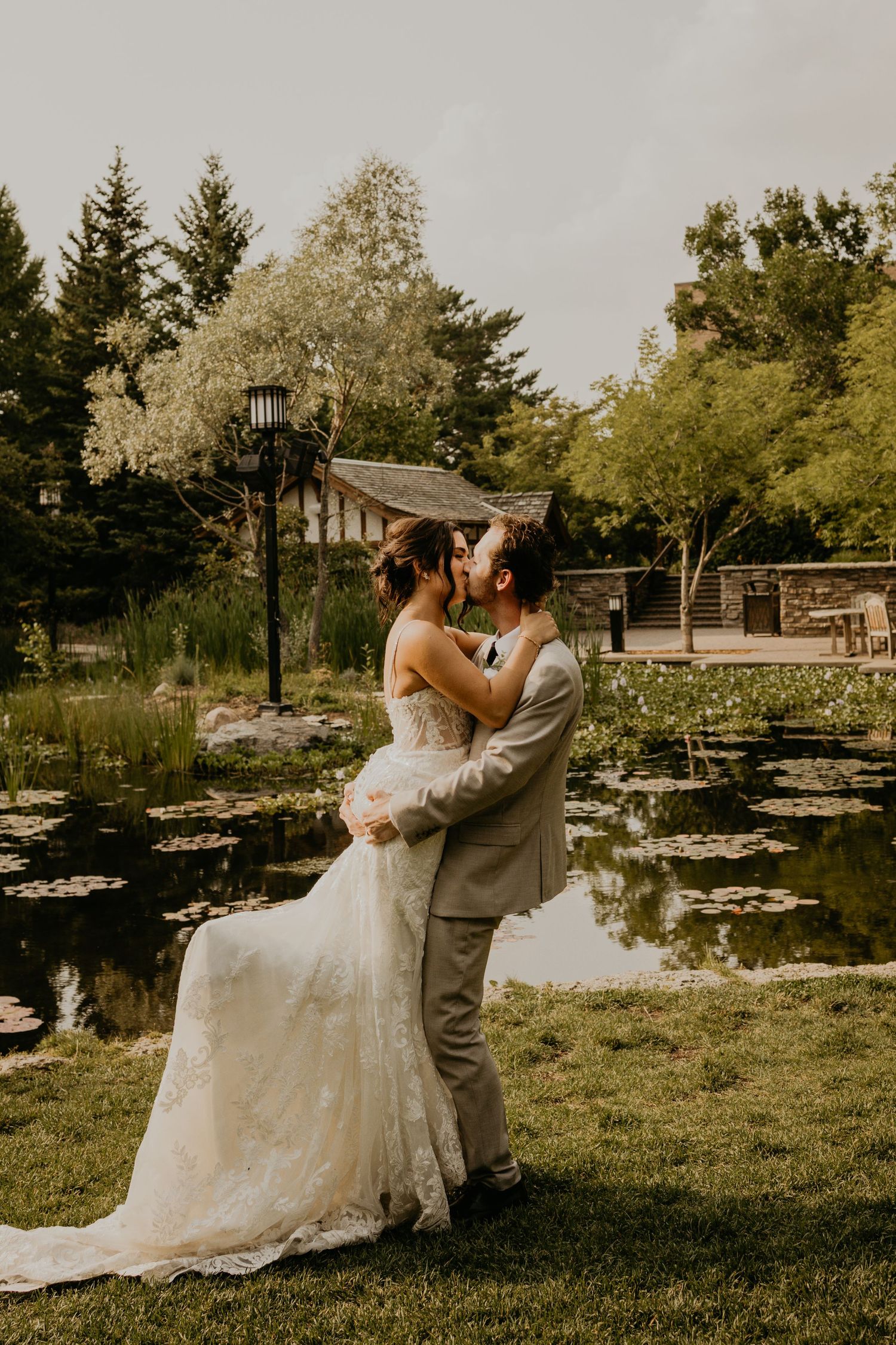 A romantic wedding portrait by a pond with lily pads and garden scenery in the background.