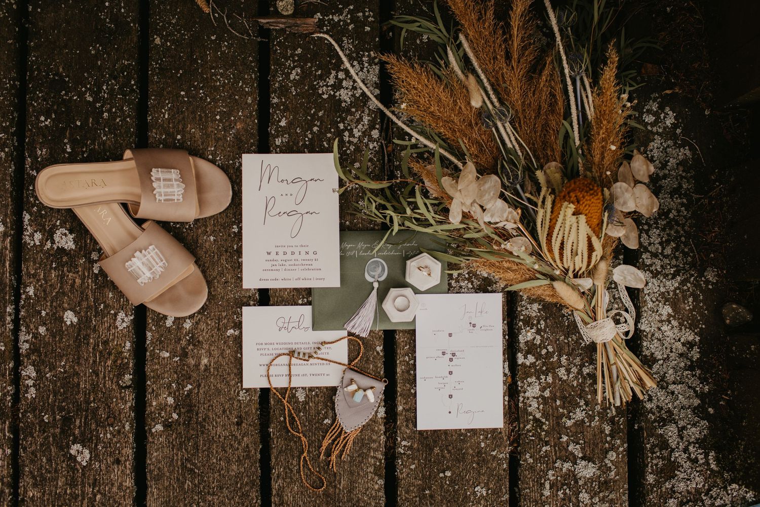 Wedding details flatlay with invitation, dried flowers and nude shoes on rustic wooden surface.