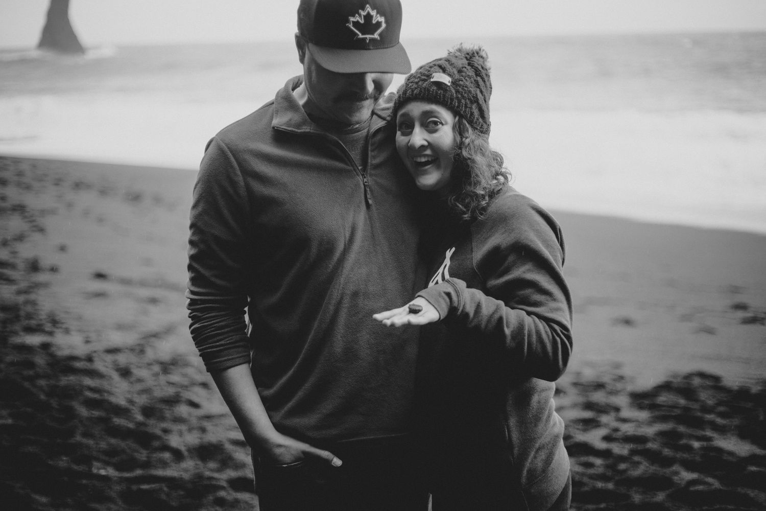 A couple in casual wear shares a candid moment while standing on a misty beach.