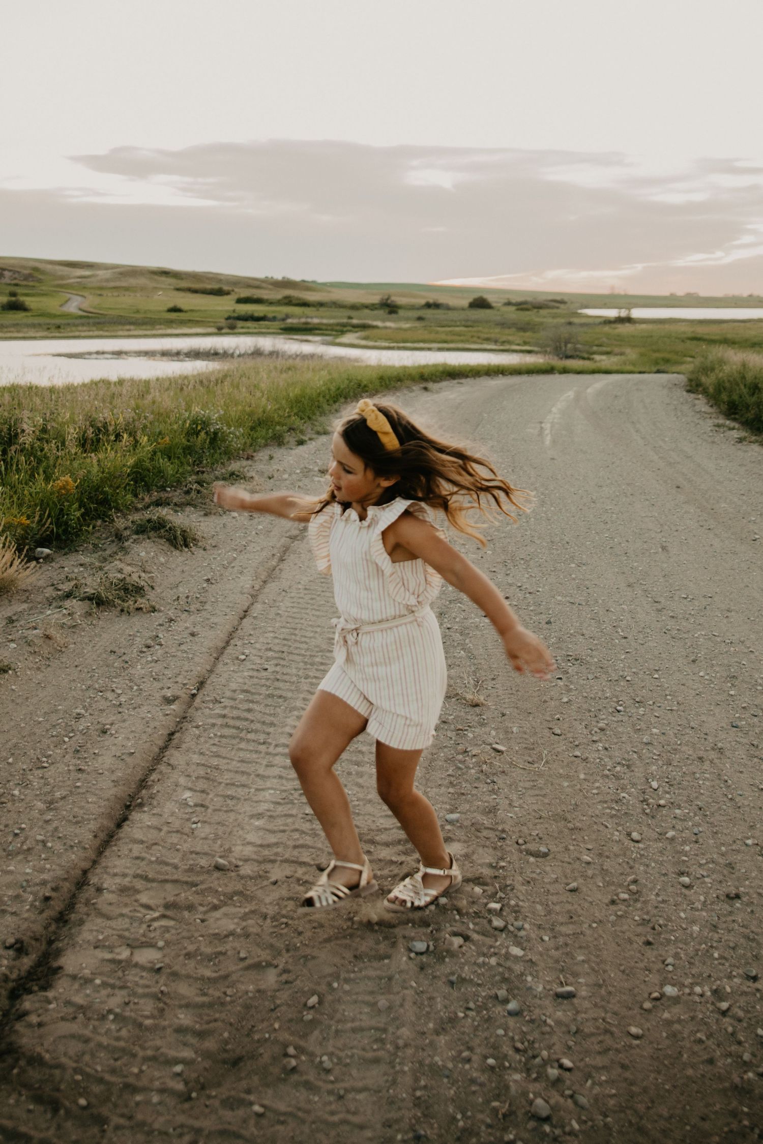 A dancing figure in a white dress spins joyfully on a dirt road at sunset.