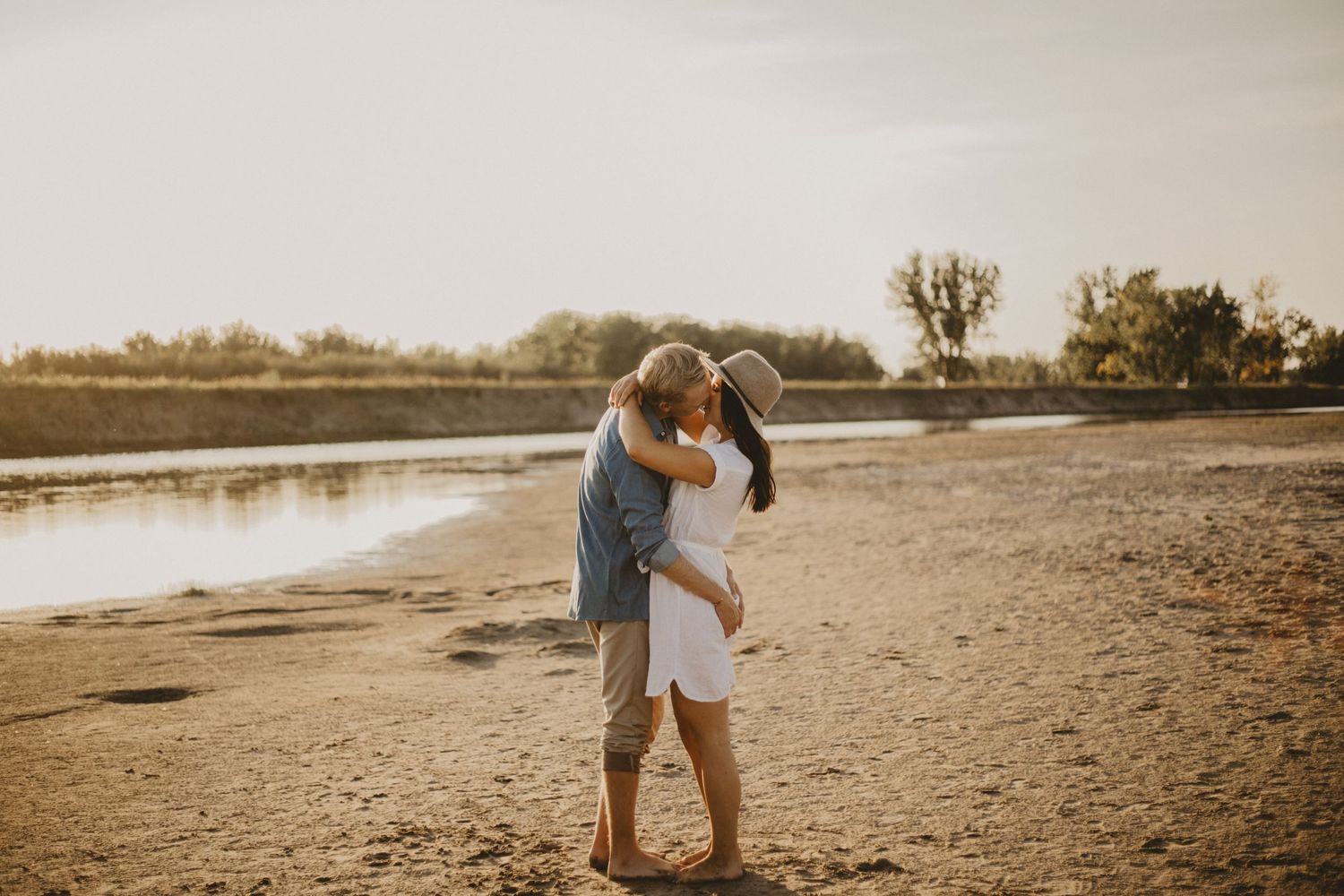 Romantic embrace on sandy beach during sunset photoshoot.