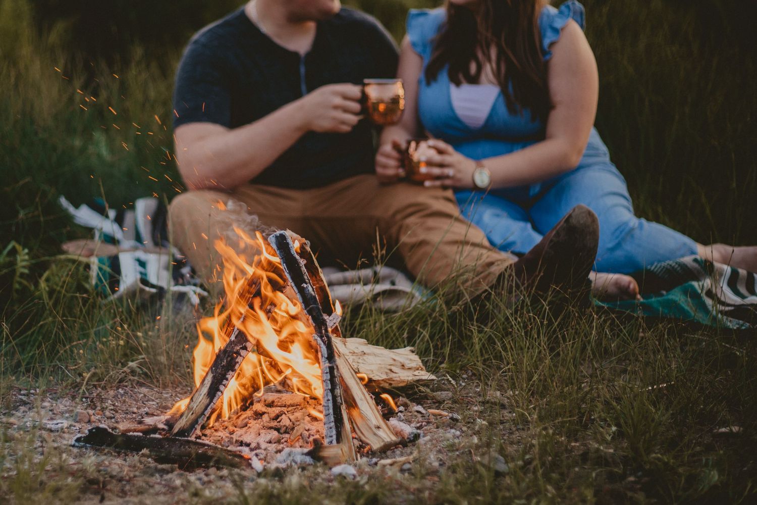 A couple sits by a warm campfire enjoying an outdoor evening together.