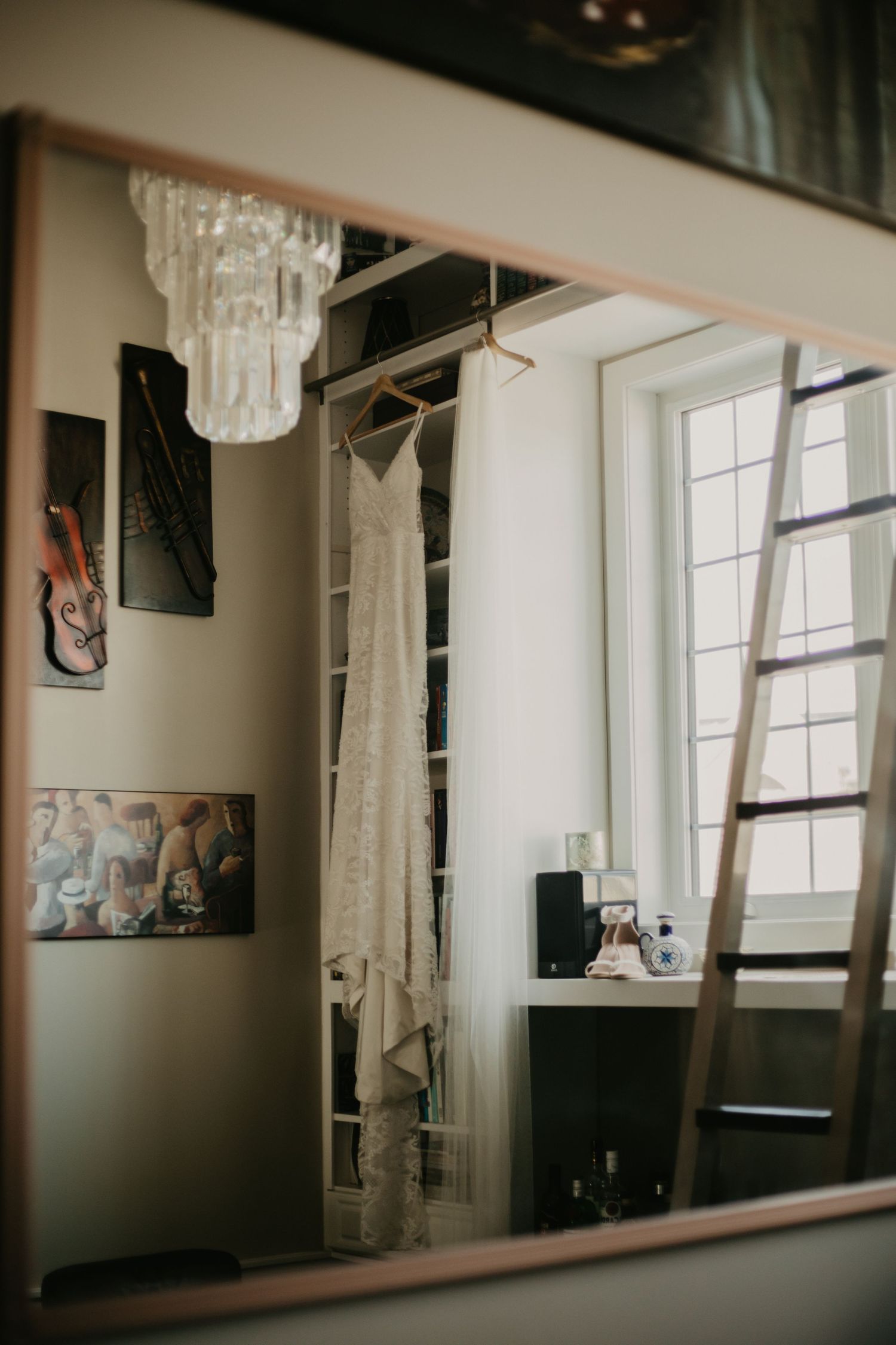 A reflection shows a wedding dress hanging in a room with built-in bookshelves and a ladder.