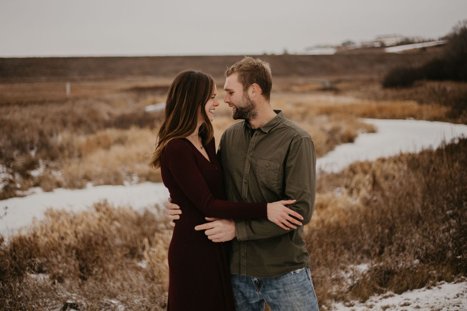 A couple shares an intimate moment in a snowy winter landscape at dusk.
