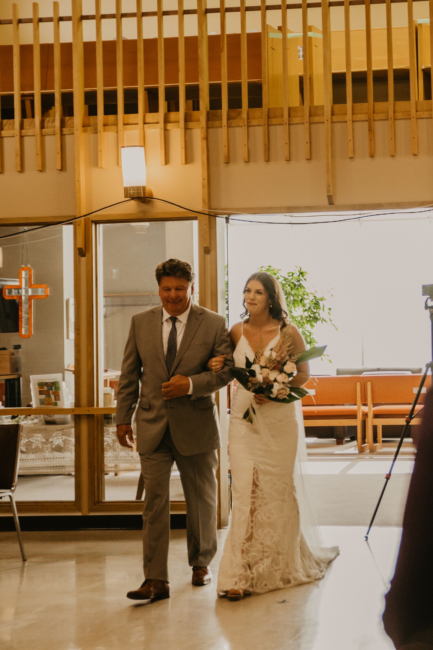 A couple walks down the aisle in a church setting with wooden lattice details overhead.