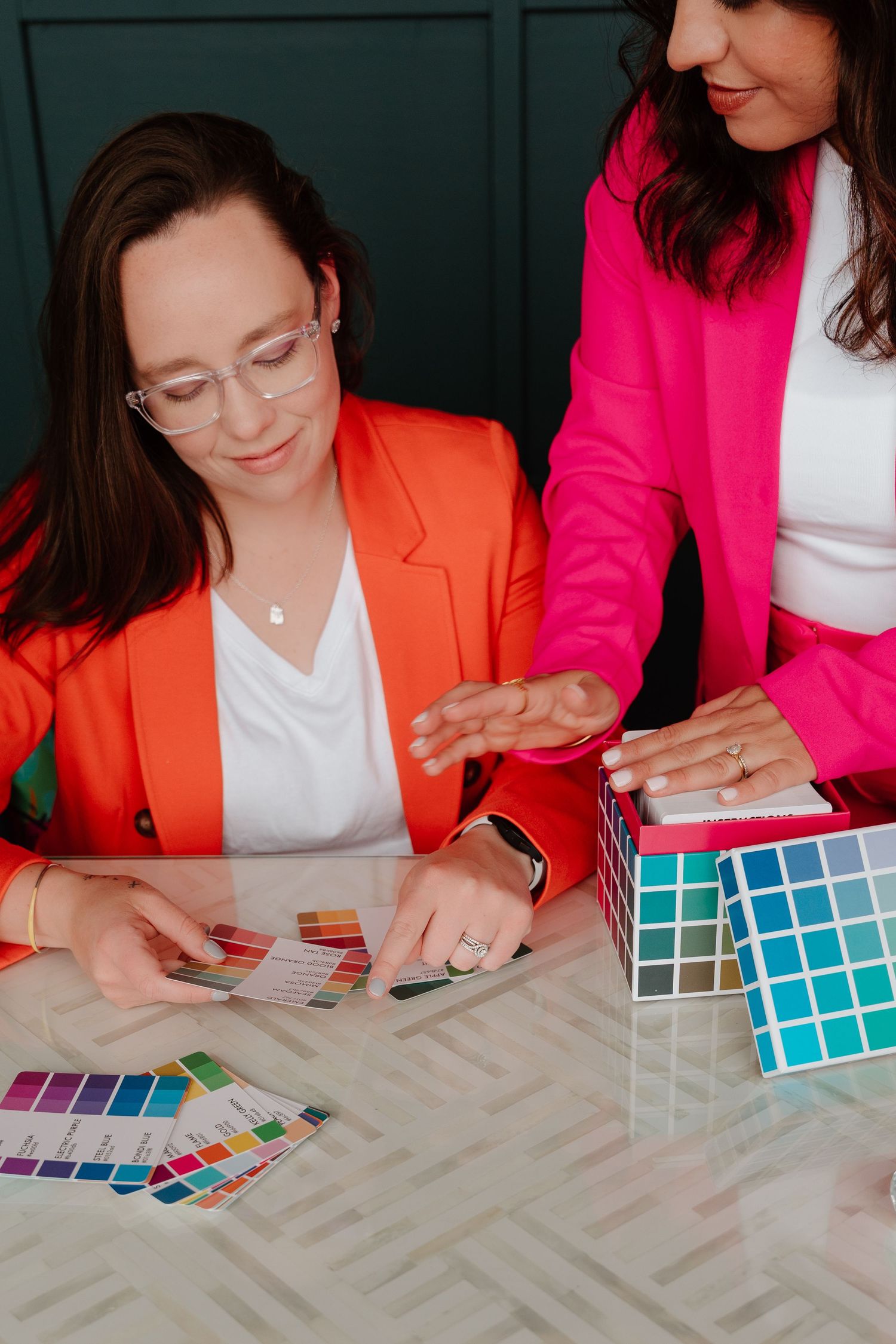 Two people in bright blazers examine color swatches and samples on a light surface.
