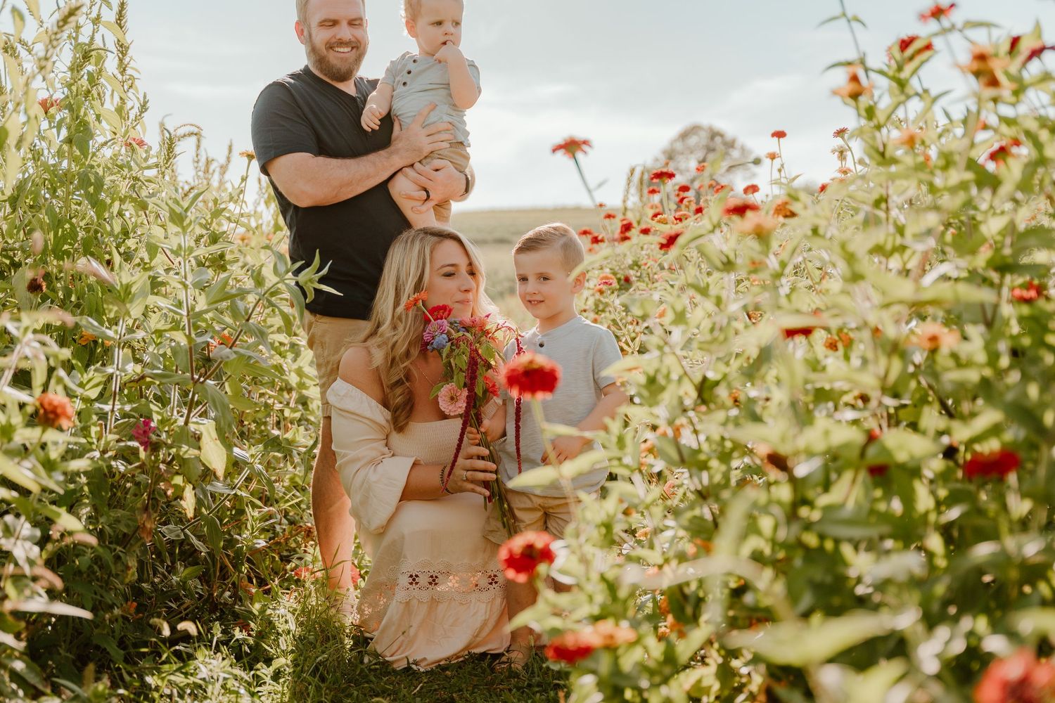 A couple and child stand together in a blooming garden with orange flowers and greenery during golden hour.
