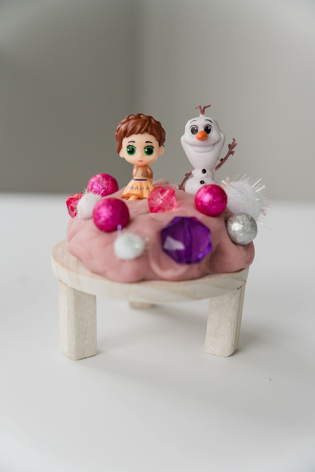 Miniature display featuring Anna and Olaf figurines with pink ornaments on a small wooden stand.