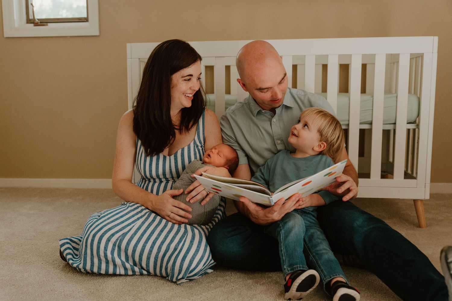 Family members sit together on a beige carpet while reading a book in a cozy living room setting.