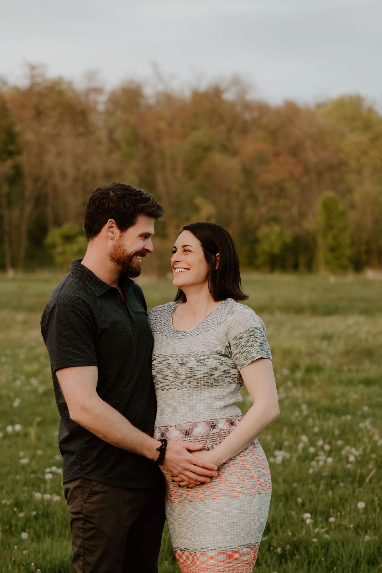 Intimate maternity photo of couple embracing in flowering meadow at sunset.
