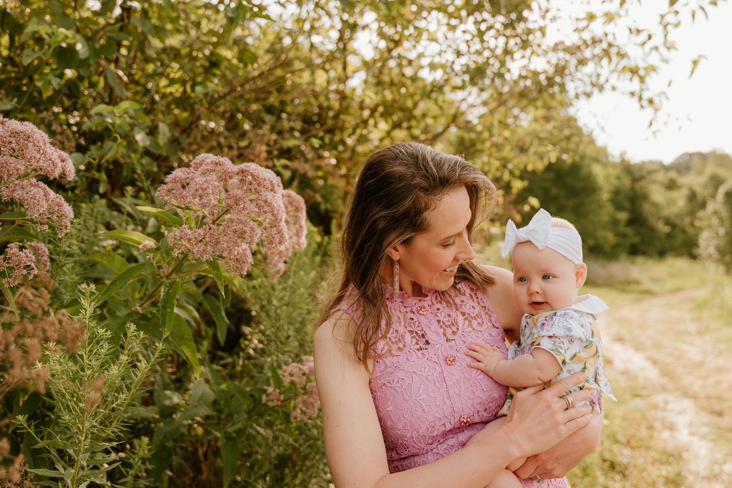 Family enjoying tender moments together outdoors in a sunlit natural setting with flowering plants.