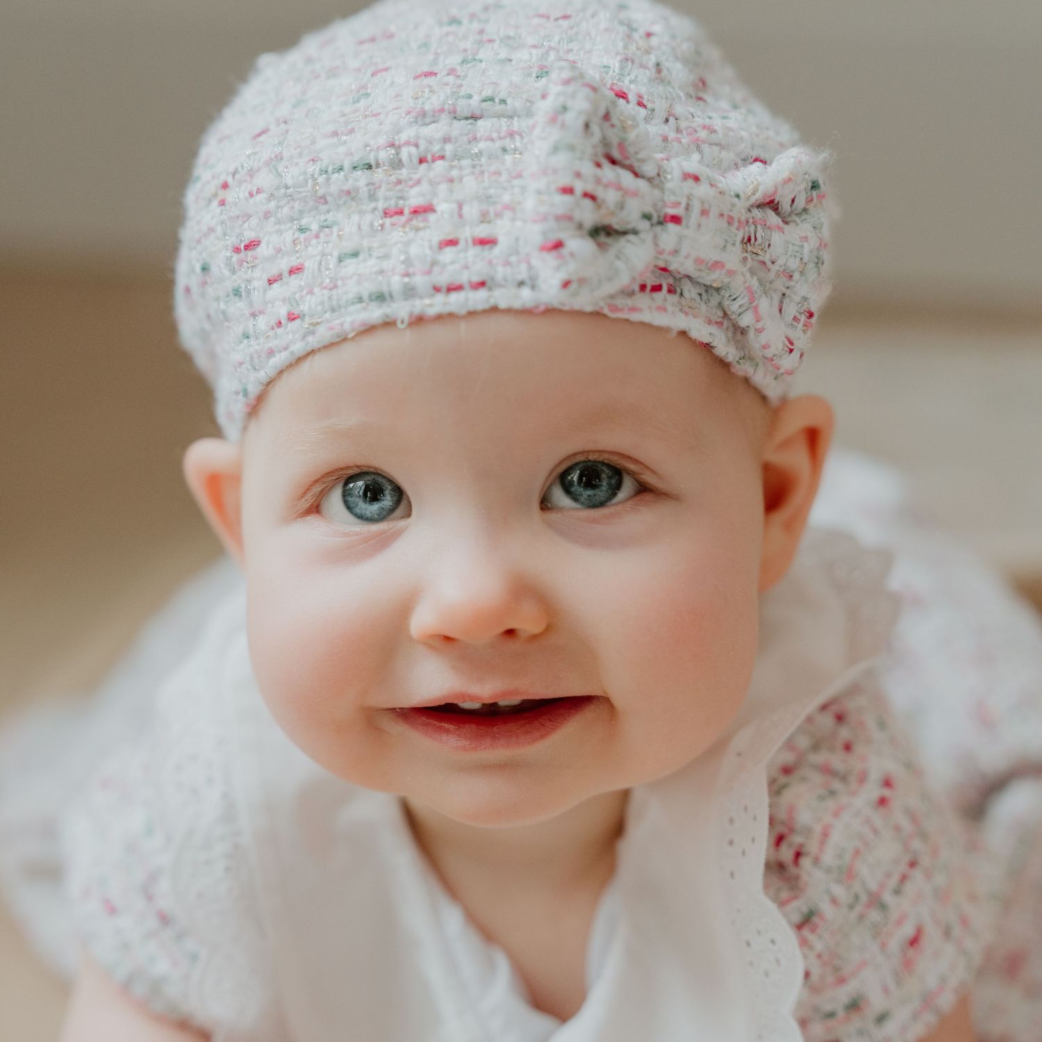 A baby wearing a delicate white floral headband and outfit smiles sweetly in a series of close-up portraits.