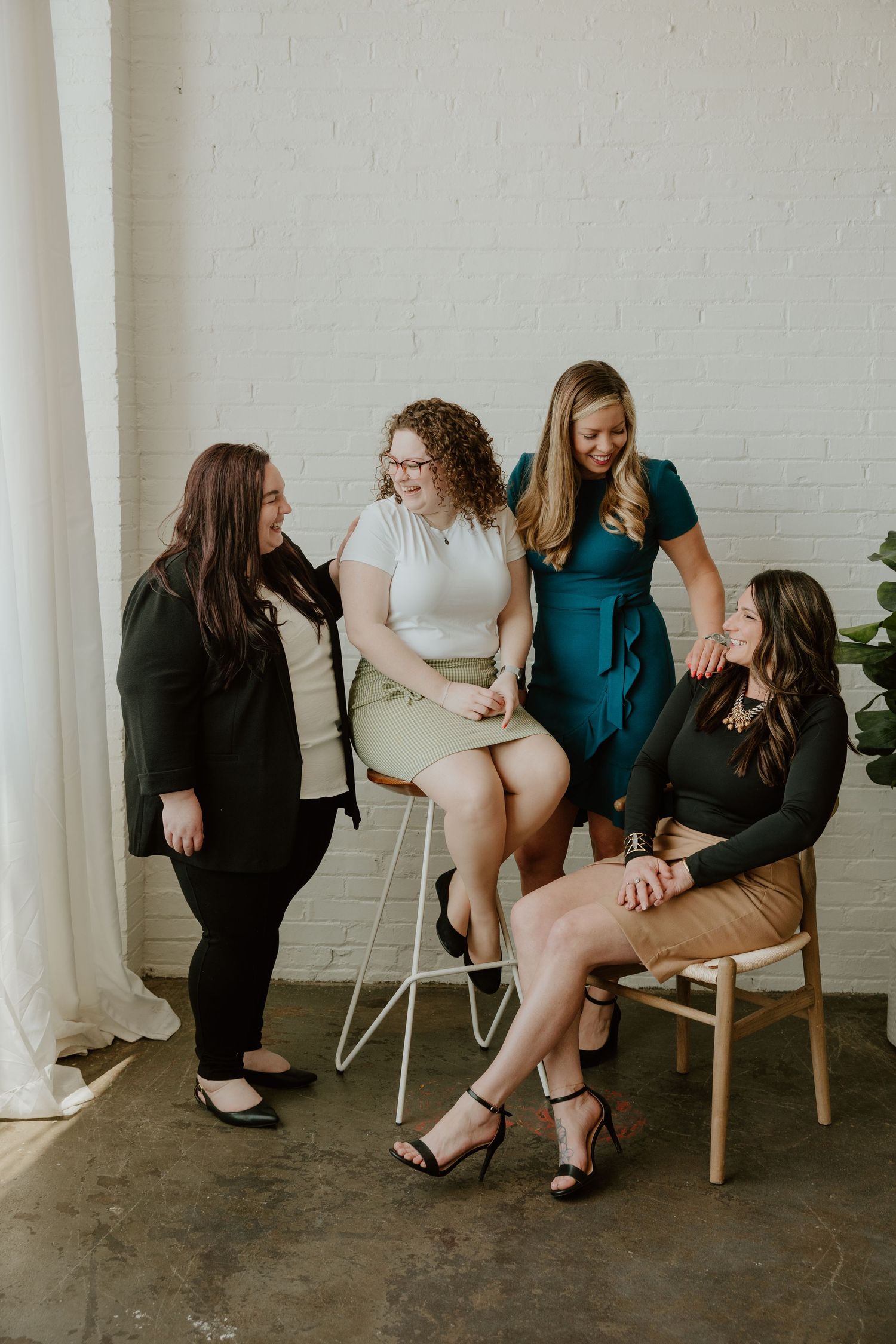 A group of women in casual attire sit and chat together in a minimalist white room with columns.