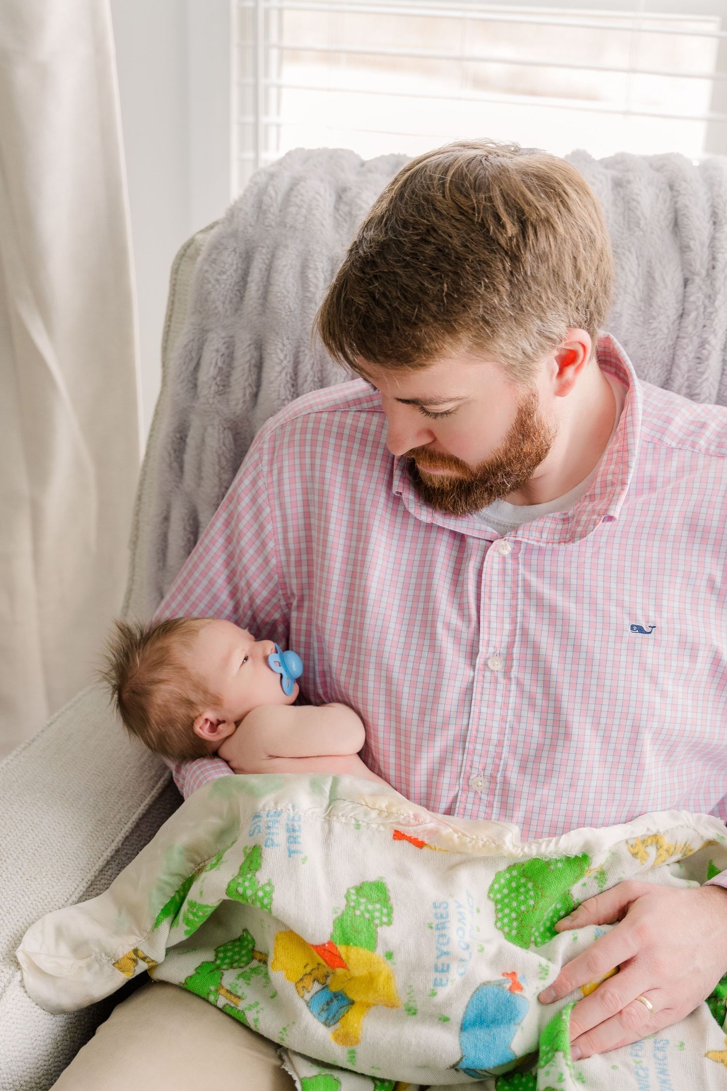 Adult holding sleeping infant wearing dinosaur print outfit in rocking chair.