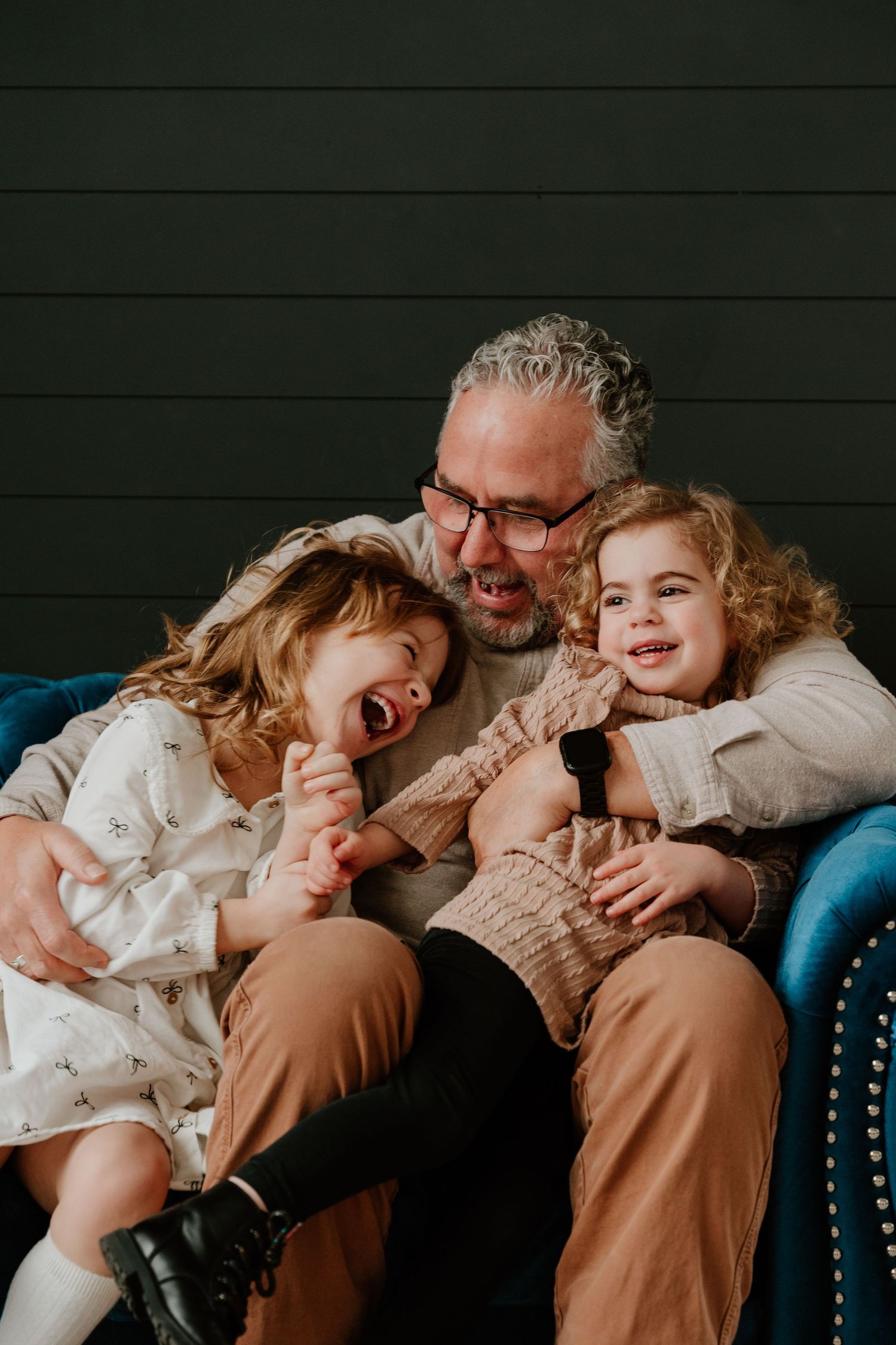 A candid moment shows a person in glasses on a blue chair sharing joyful laughter with two children.