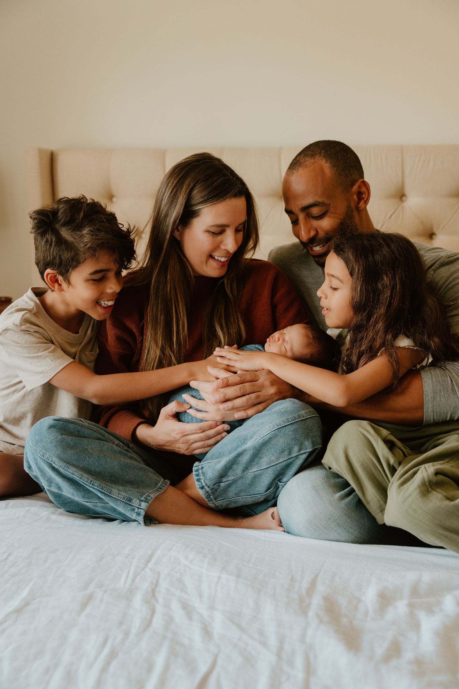 A loving family of five cuddles together on a beige couch while bonding with their newborn baby.