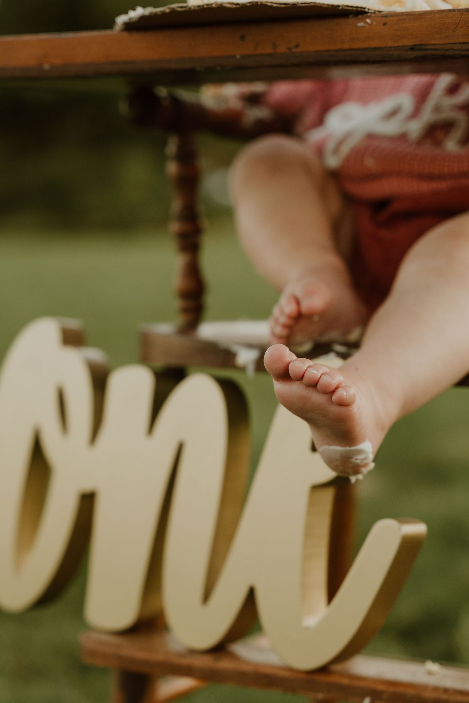 Close-up of tiny feet resting on wooden high chair with 'ONE' text decoration.