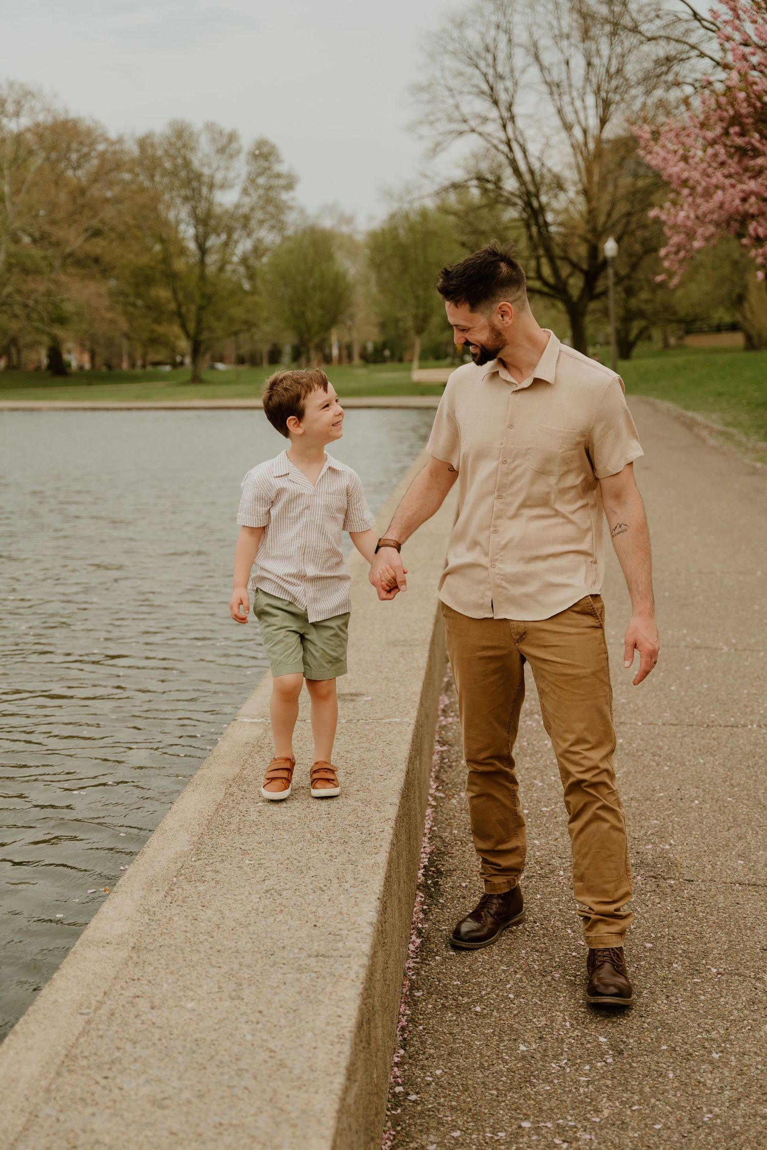 People walking along a lakeside path kick up water from puddles during a spring day at the park.