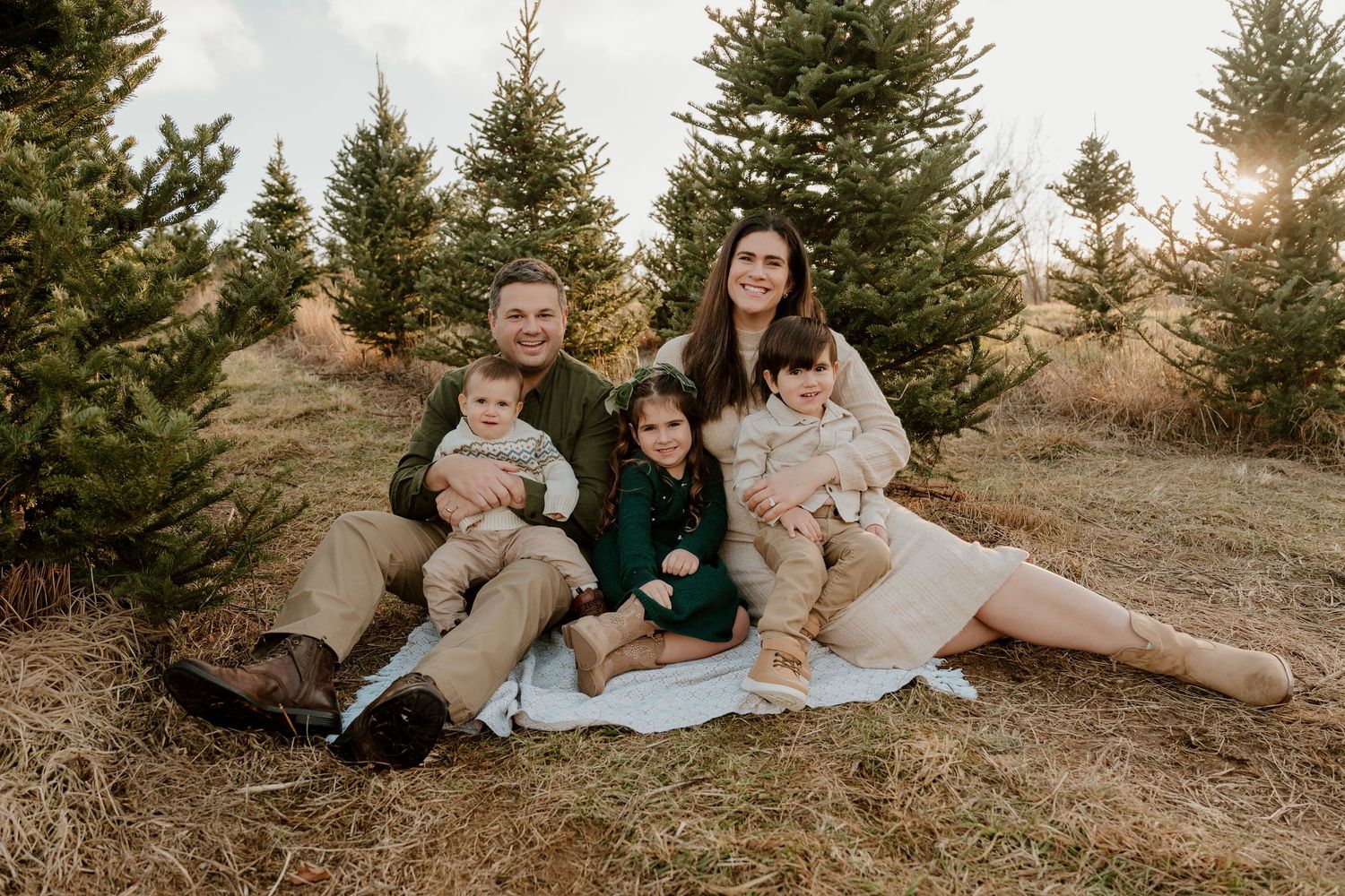Family relaxing together on a grassy hillside surrounded by evergreen trees during golden hour sunset in Washington, PA