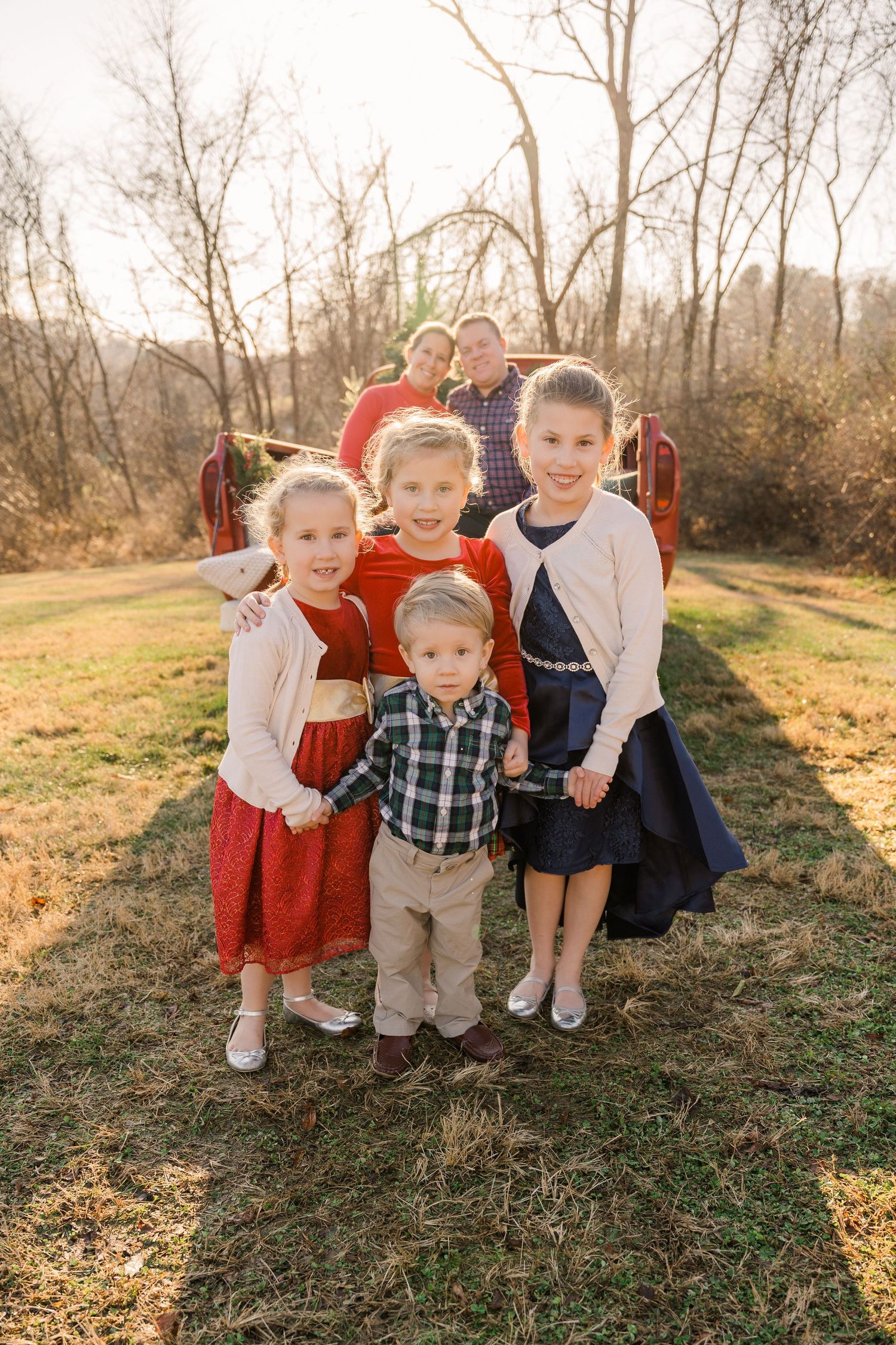 Group of children in dressy attire pose together outdoors near vintage truck.