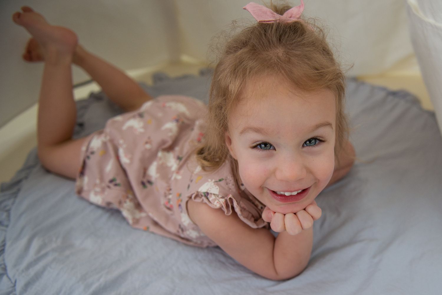 Child lying on gray bedding wearing pink floral dress.