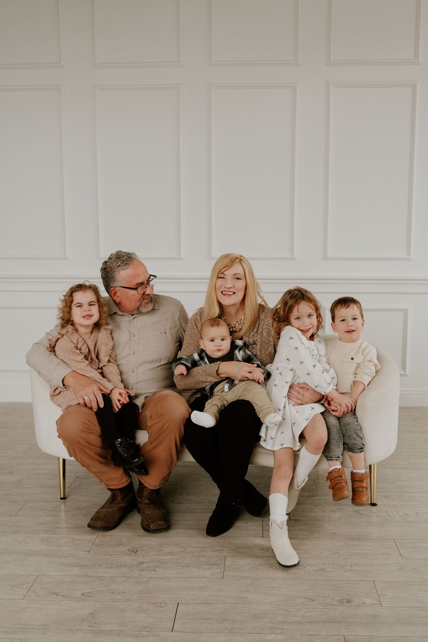 Family sitting together in a row against white wall wearing coordinated brown and neutral colored outfits for portraits.