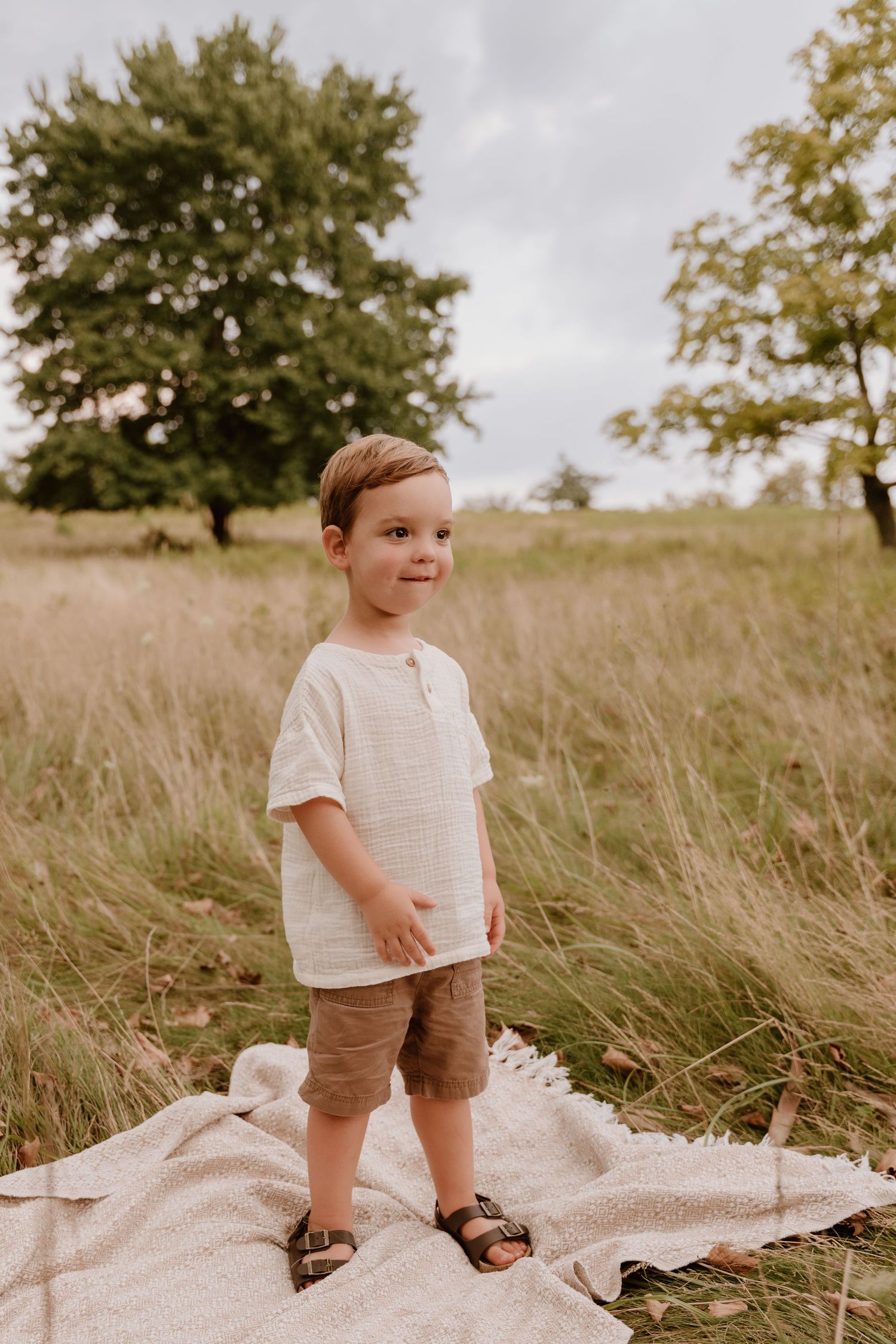 Young child standing on blanket in tall grass field during golden hour.