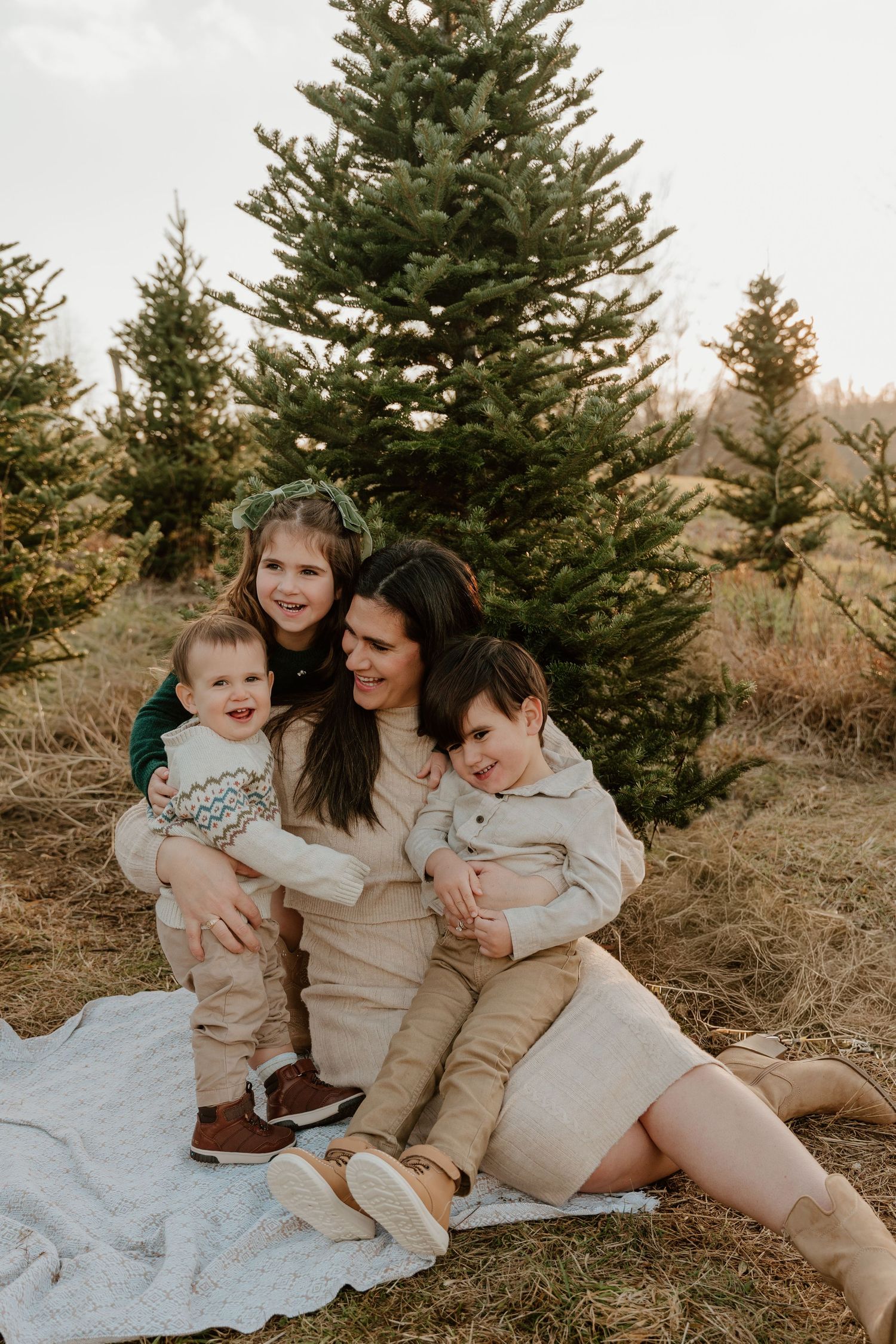 A family sits together on a blanket in front of evergreen trees during a cozy outdoor photo session.