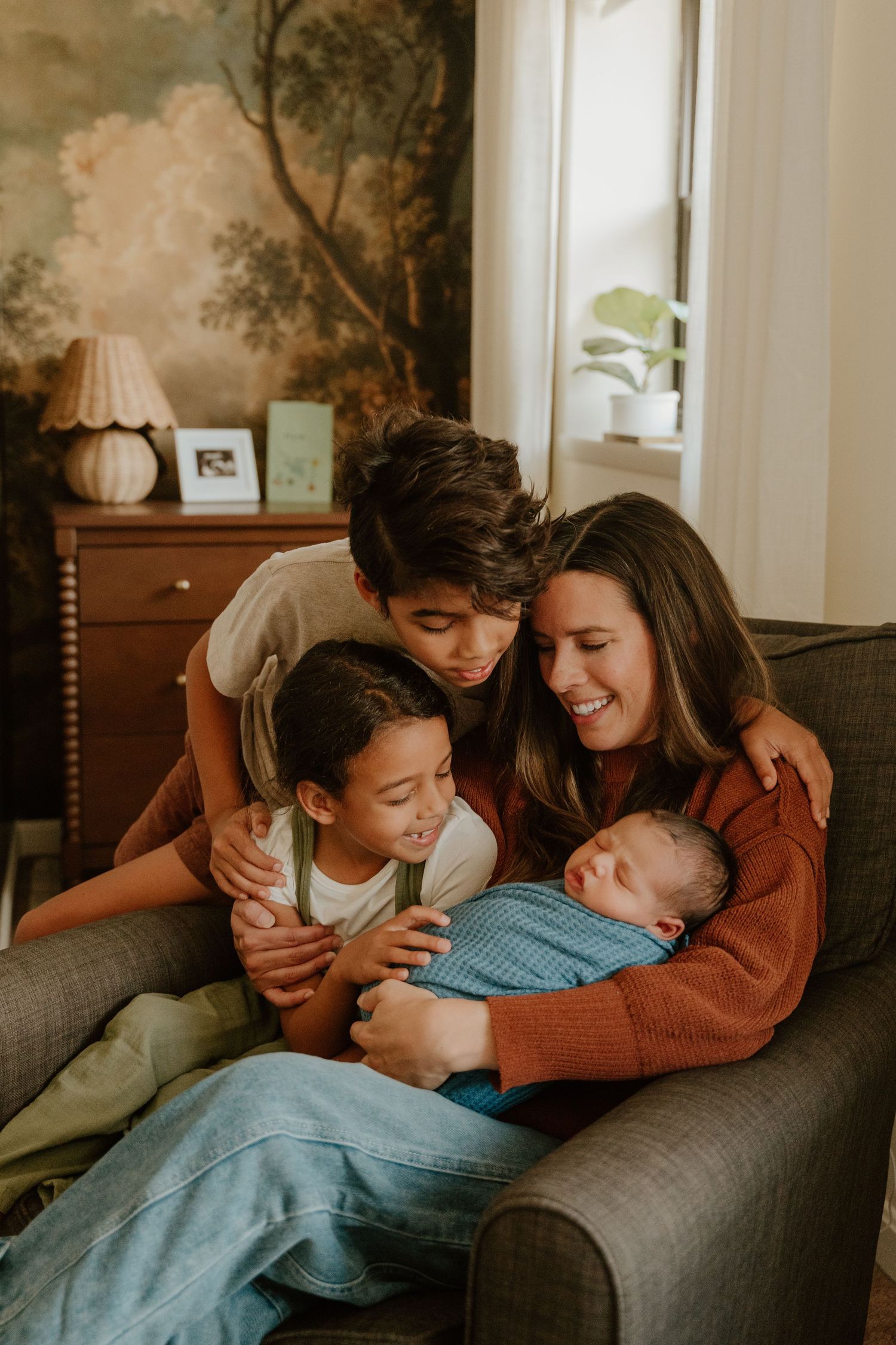 A family shares a tender moment together while cuddling on a gray couch in a sunlit living room.