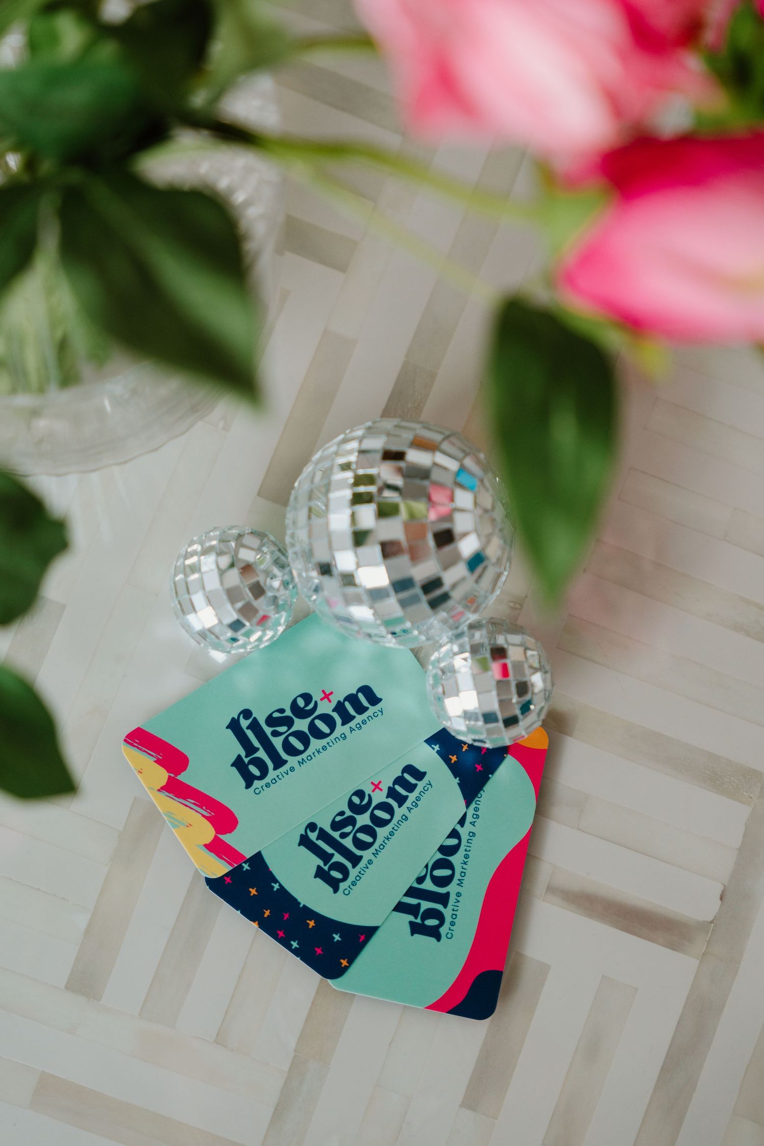 Disco ball ornaments and teal-colored cards with pink accents arranged in a sequence against a white background.