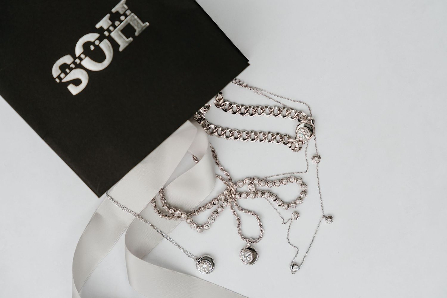 Silver jewelry pieces including necklaces, earrings and bracelets displayed on white surface with black packaging.