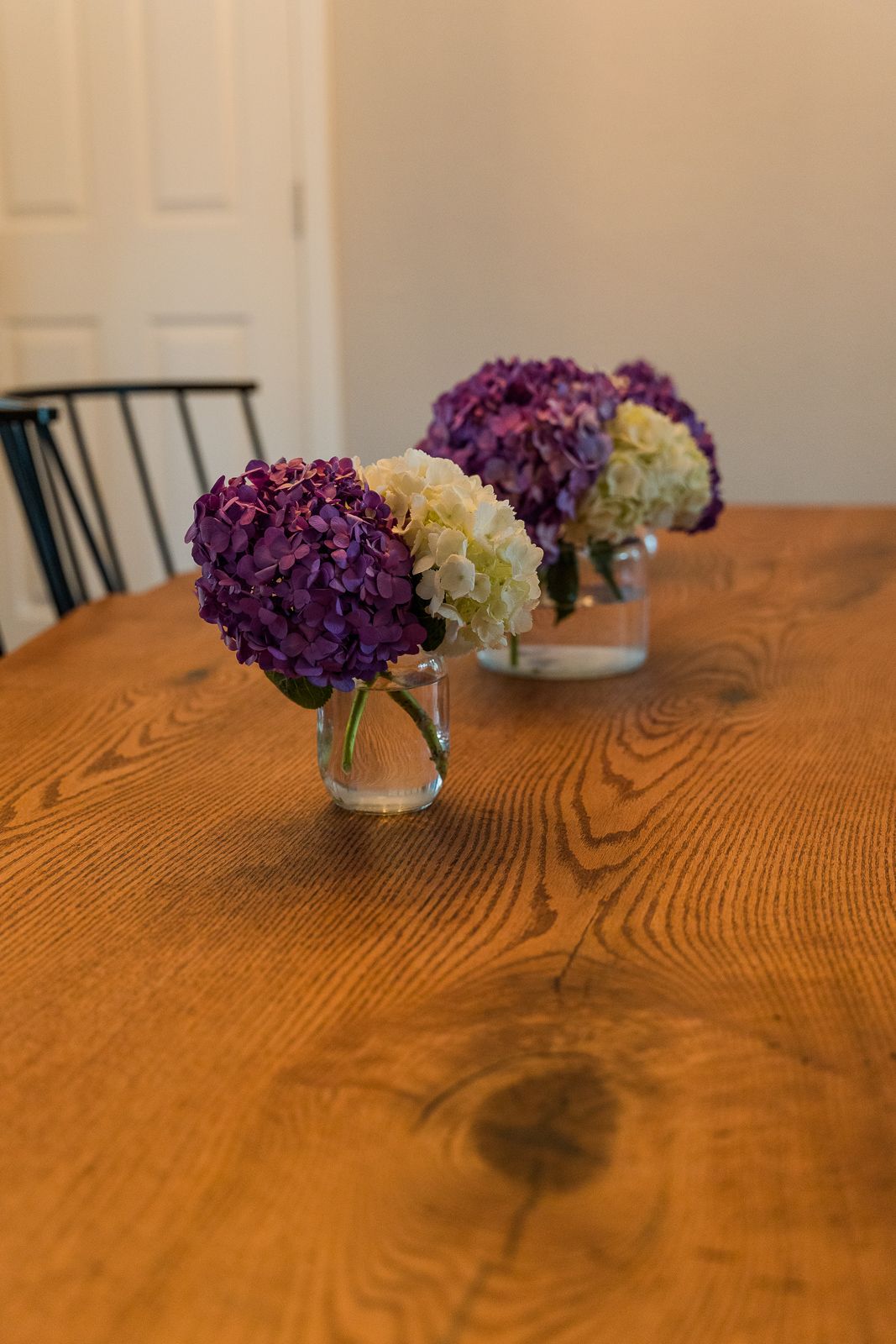 Purple and cream hydrangea centerpieces in glass vases on wooden table.