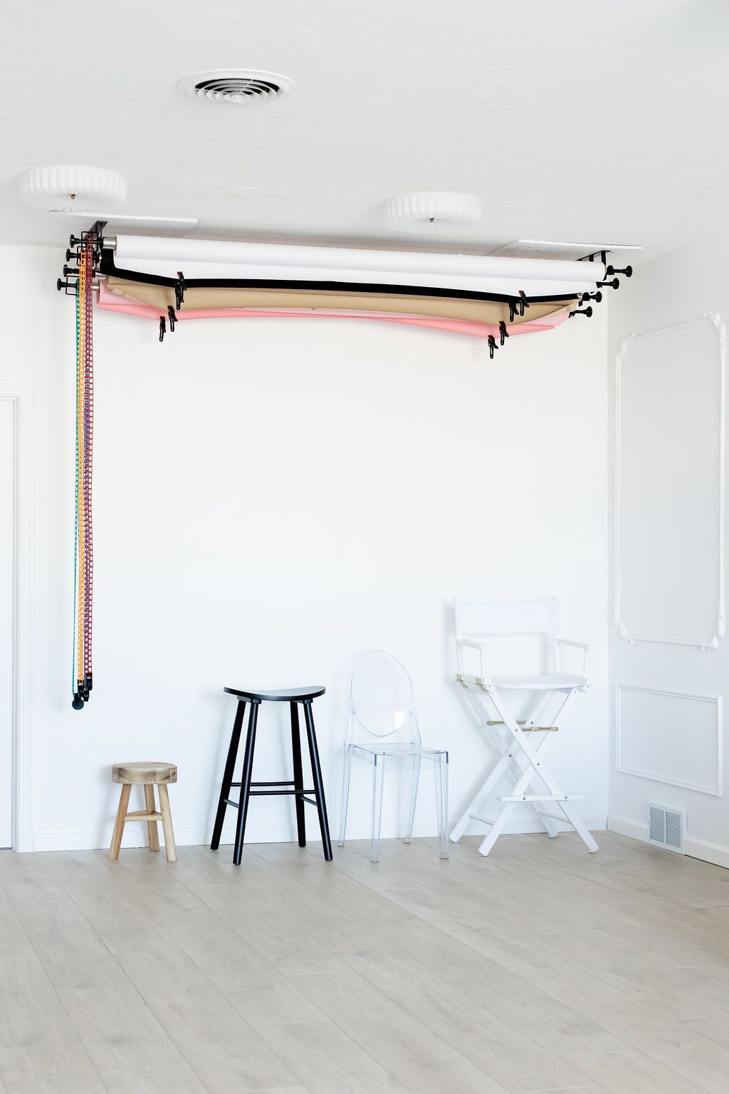 A minimalist white photography studio space with wooden stools and a professional lighting setup mounted on the ceiling.