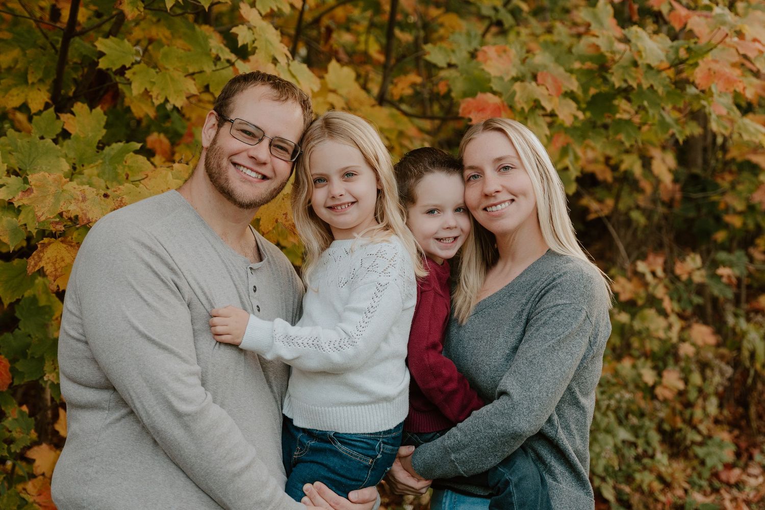 A happy family poses together outdoors against autumn foliage with colorful fall leaves in the background.