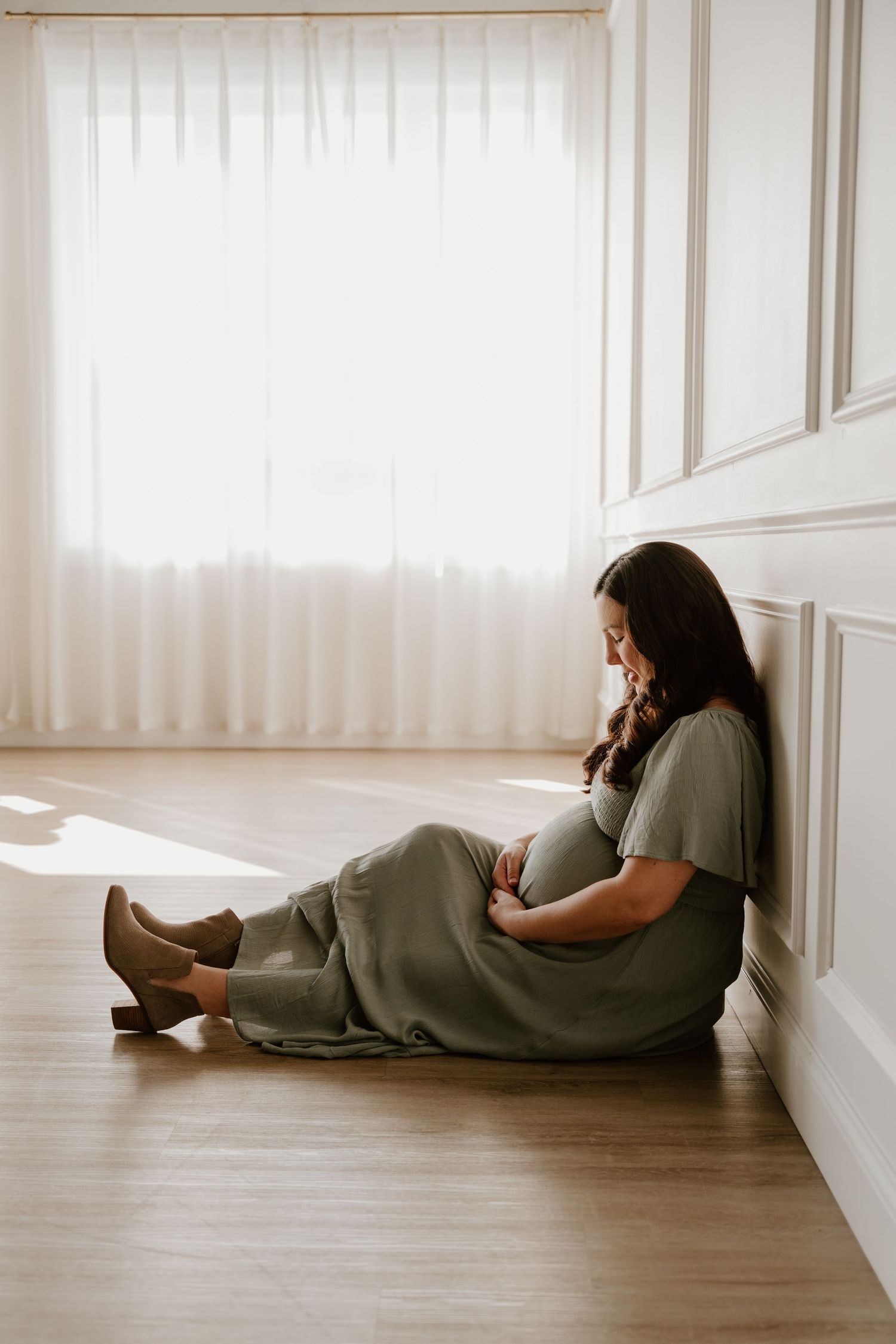 Person in grey loungewear lying on wooden floor against white wall while using mobile phone.