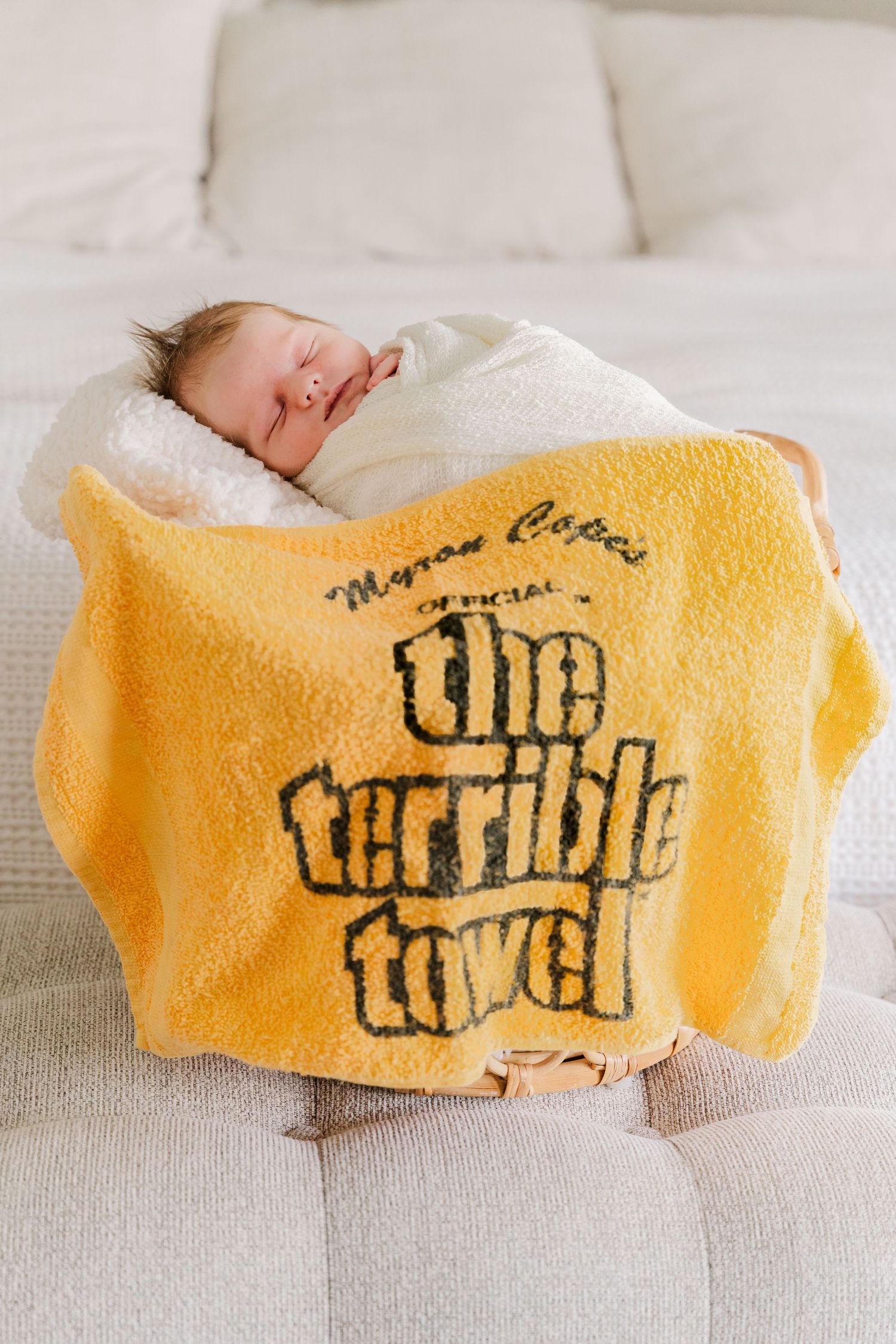 Sleeping baby wrapped in white blanket with yellow Terrible Towel blanket.