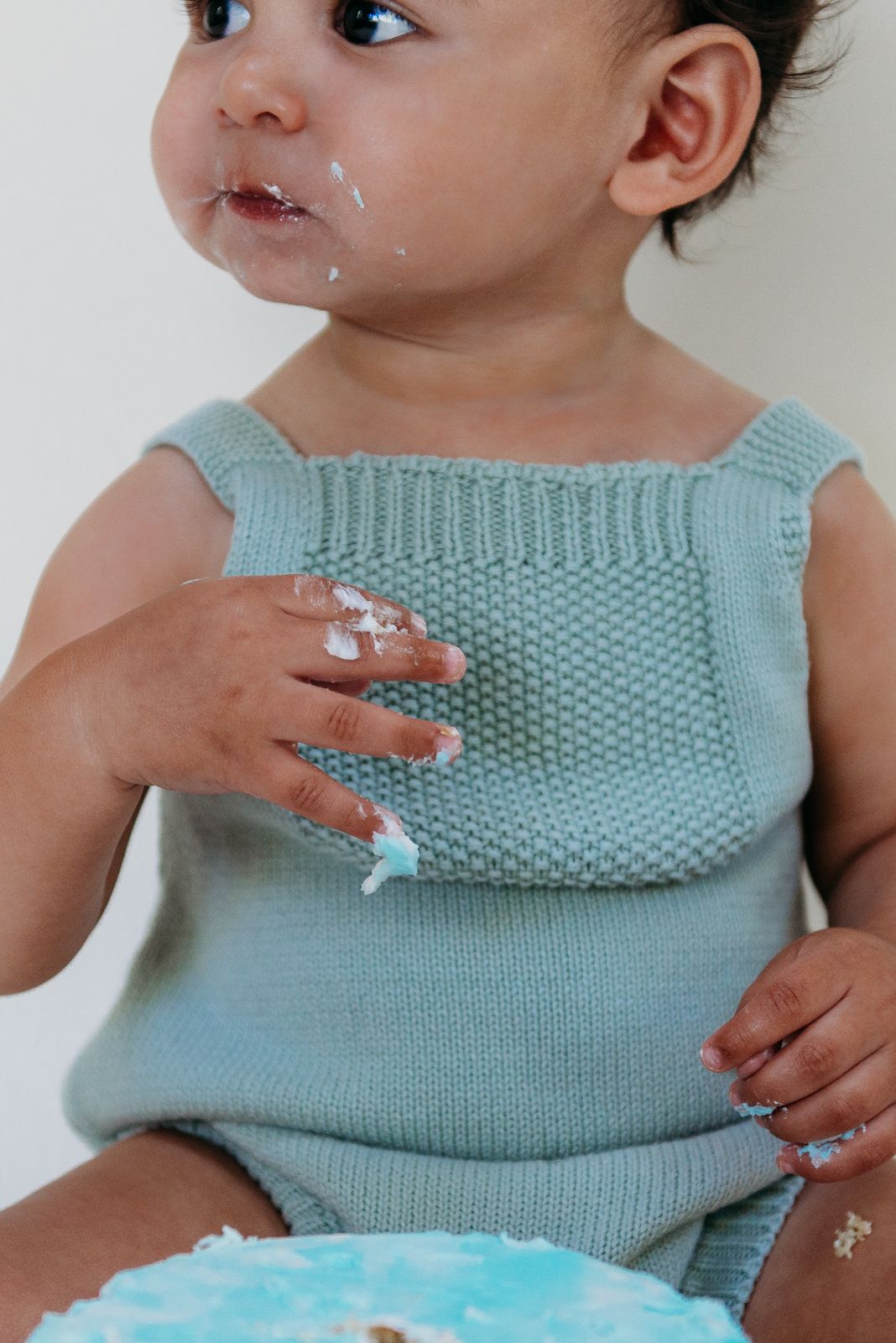 Close up of messy baby hands and face after eating birthday cake.