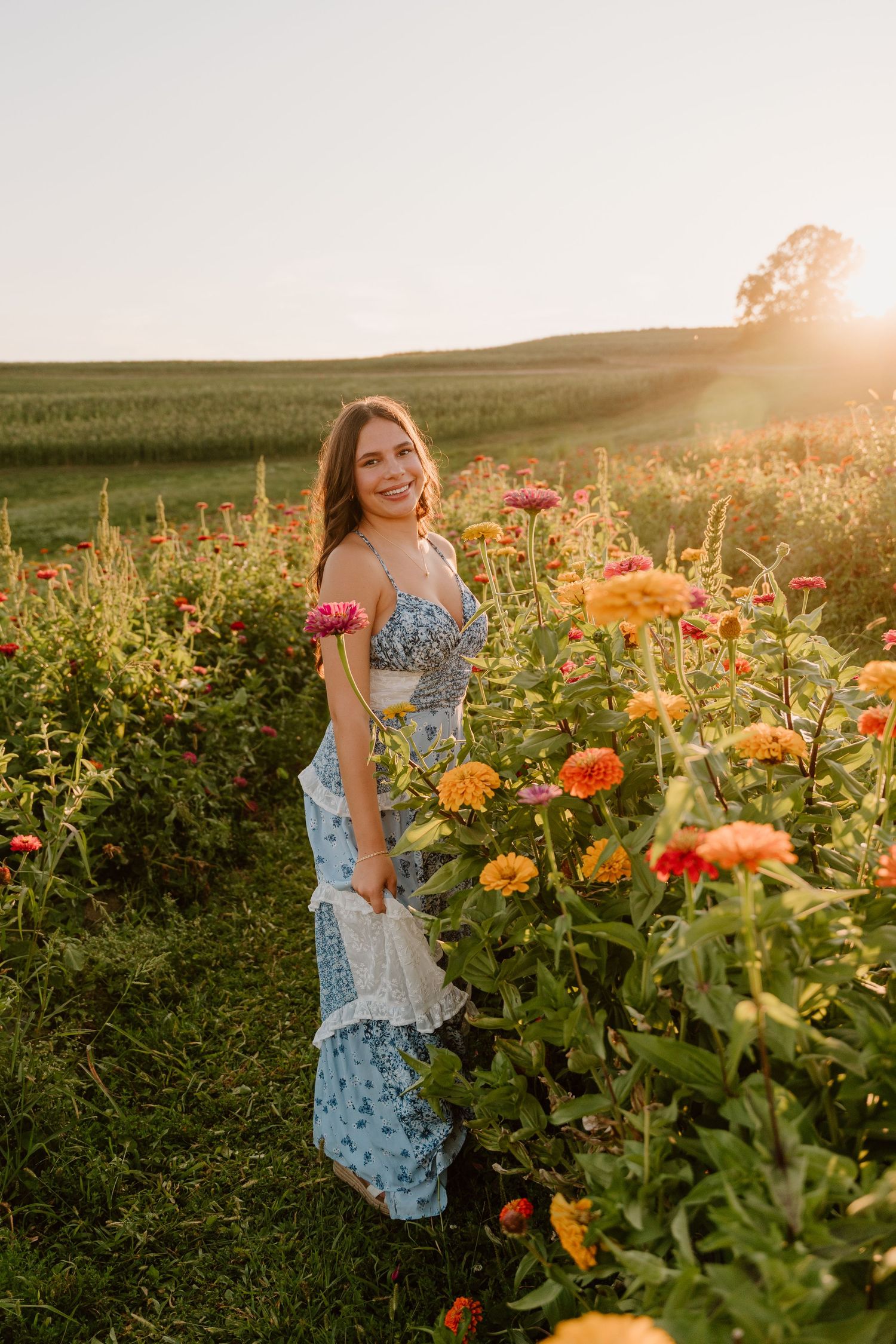 A woman in a blue floral dress walks through a vibrant flower garden at golden hour sunset.